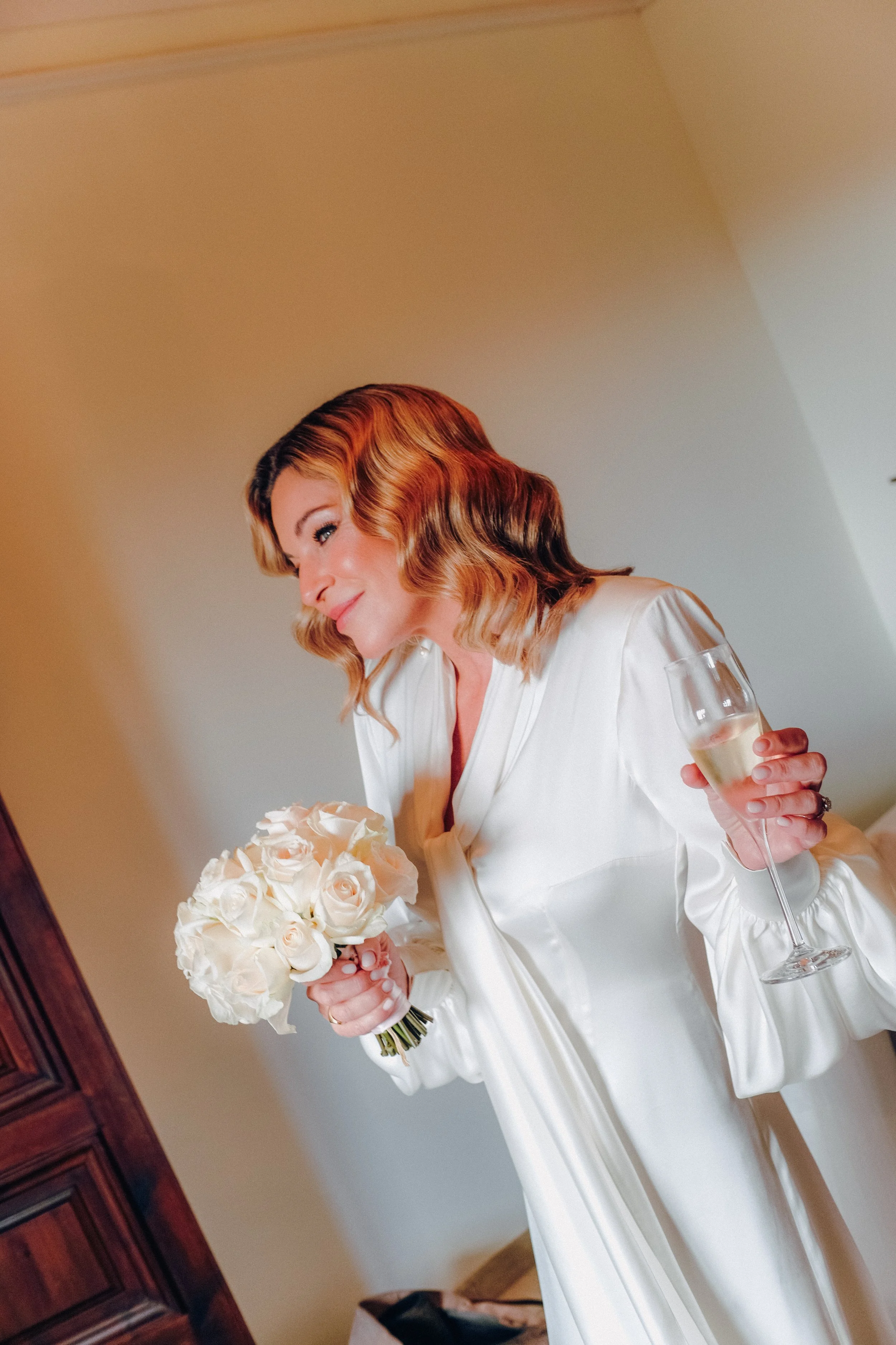 Mujer con vestido blanco sosteniendo un ramo de rosas y una copa de champagne.