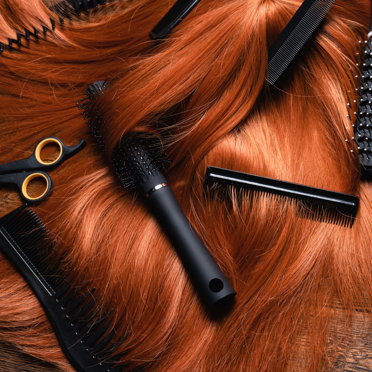 Cabello rojo y herramientas de peluquería como peines, tijeras, rulos y cepillos en una mesa.