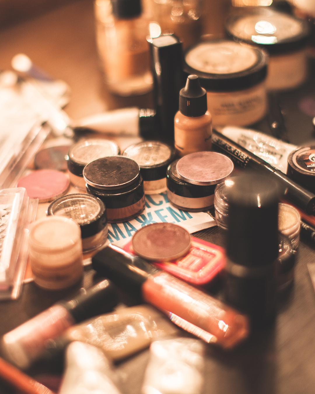 Diversos productos de maquillaje, incluyendo botes de crema, pigmentos, y aplicadores sobre una mesa.