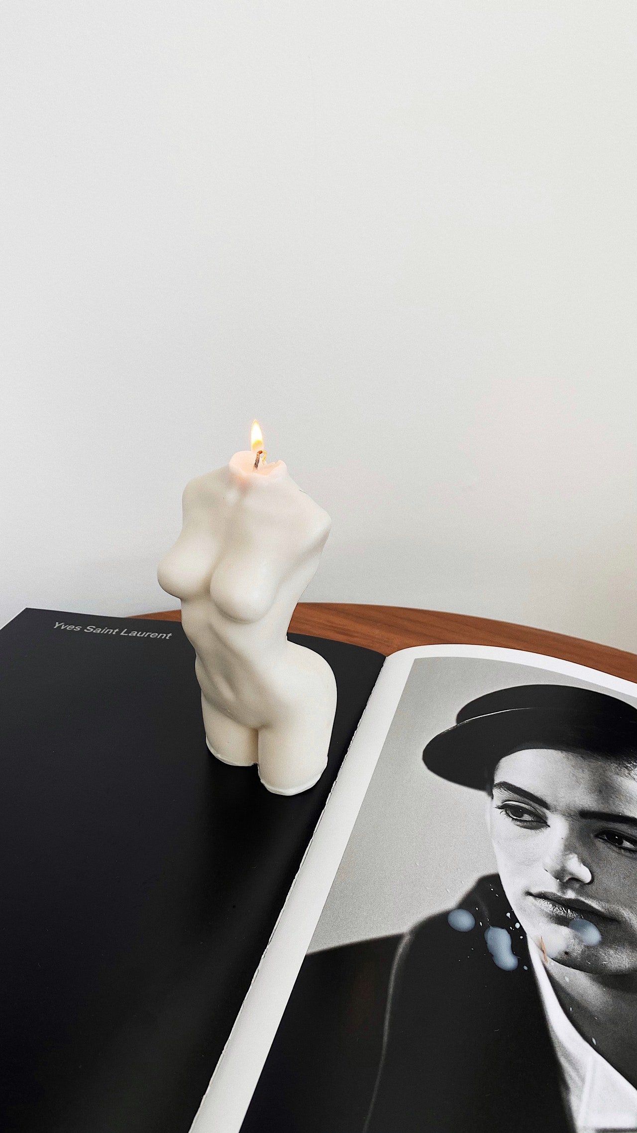 A candle shaped like a woman's torso with a flame on top, placed on an open book with black and white photo of a woman wearing a hat.