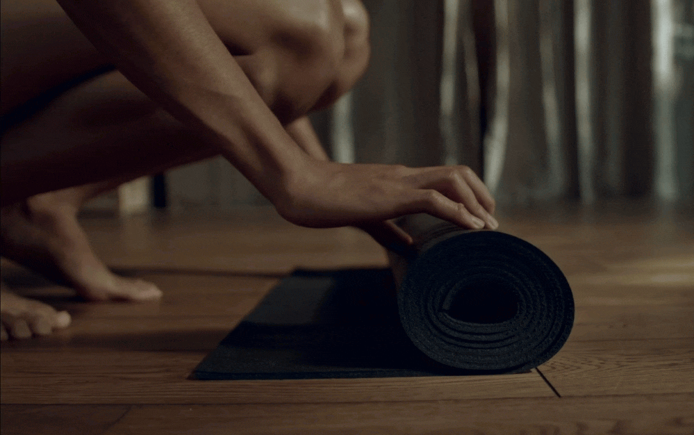 A person is rolling out a black yoga mat on a wooden floor.