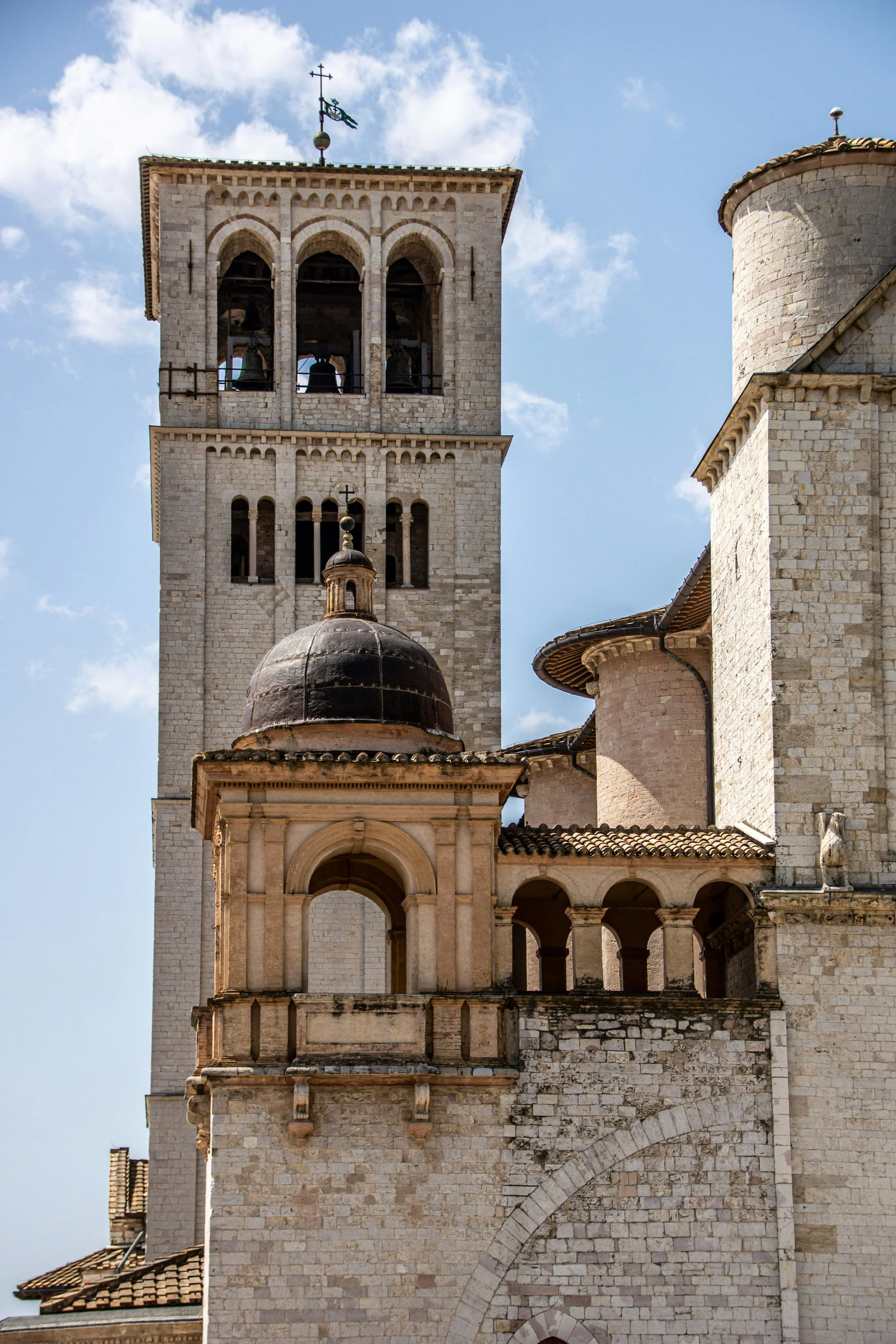 View of an old stone church with a bell tower and a decorative dome, against a background of blue sky with clouds.