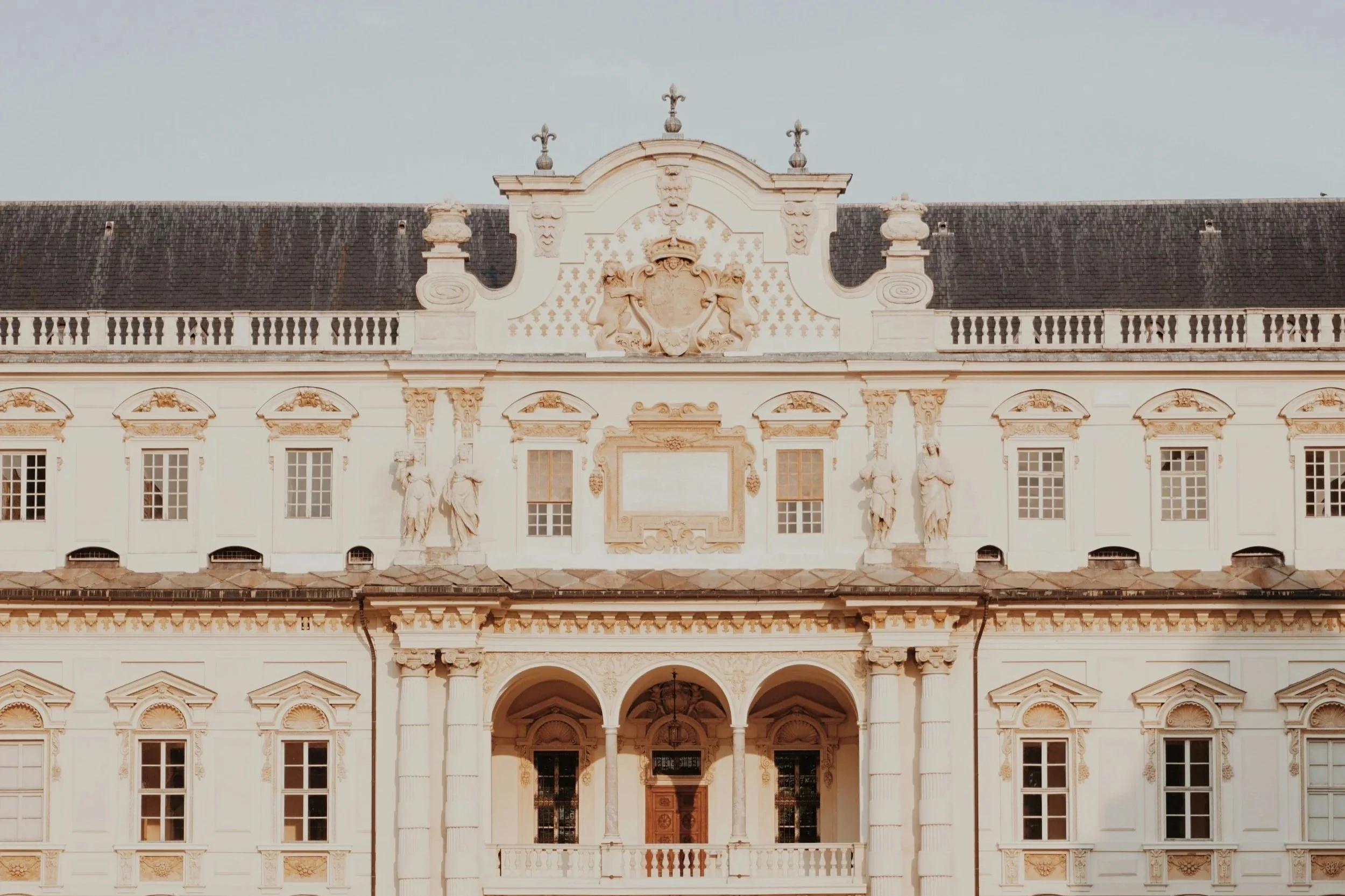 The front of an ornate historic building with Baroque architectural features, including decorative sculptures, columns, and a gabled roof with statues.