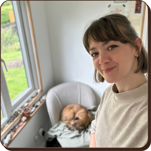 EJ facing the camera smiling with pippin the border terrier in the background curled up asleep on the chair.