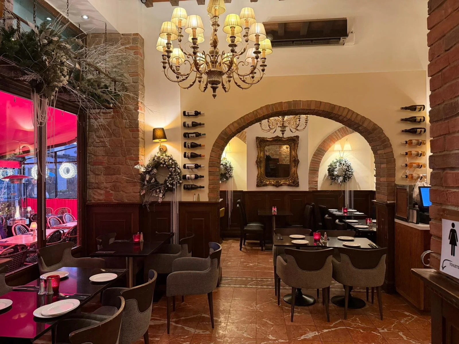 Interior of a restaurant decorated for Christmas with wreaths, wreaths, and a chandelier, with tables set for dining.