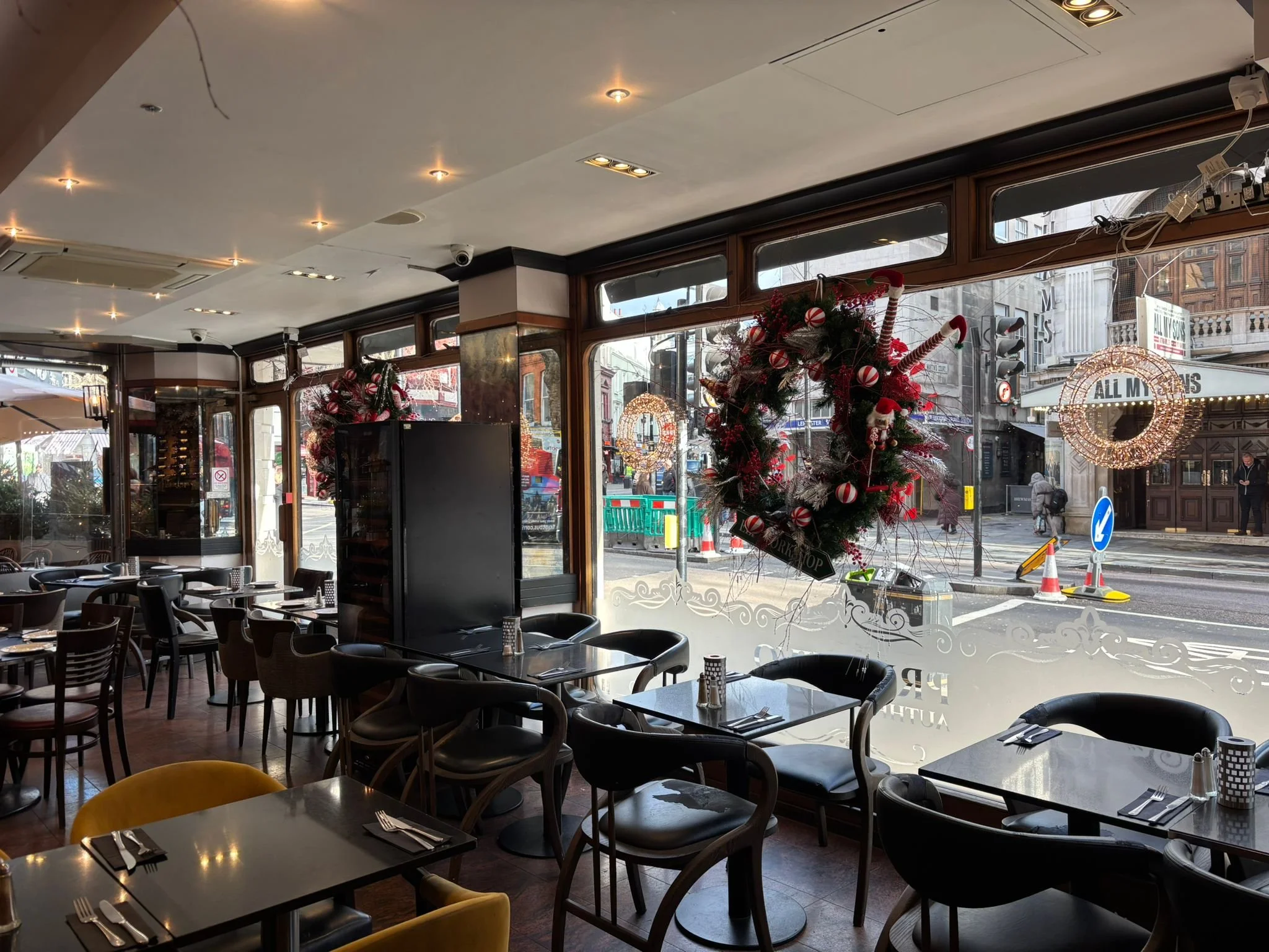 Interior of a restaurant decorated for Christmas, featuring a large Christmas wreath with candy canes and ornaments hanging in the window.