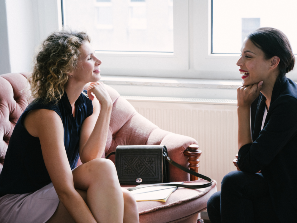 Zwei Frauen führen ein Gespräch in einem hellen Raum.