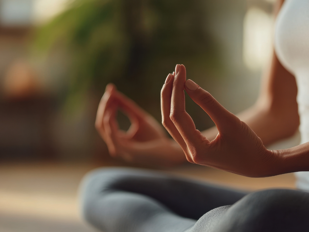Person, die in einer Meditationshaltung sitzt und die Hände im Mudra hält, mit Fokus auf die Handhaltung, im Innenbereich mit natürlichem Licht.