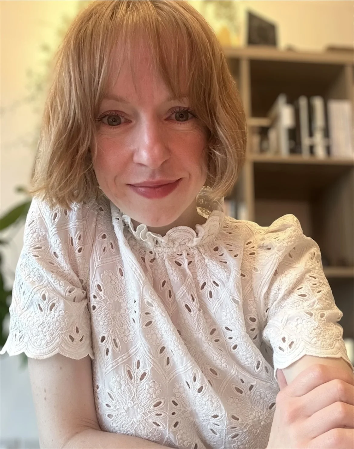 A photo of Frances Jenkins, founder of Roar at the World. She is in front of a bookcase and plants and is leaning towards the camera smiling
