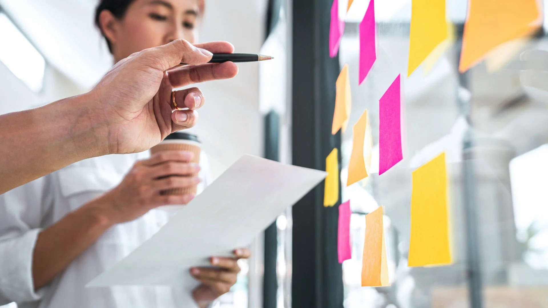 People reviewing sticky notes on a glass wall while holding coffee cups.