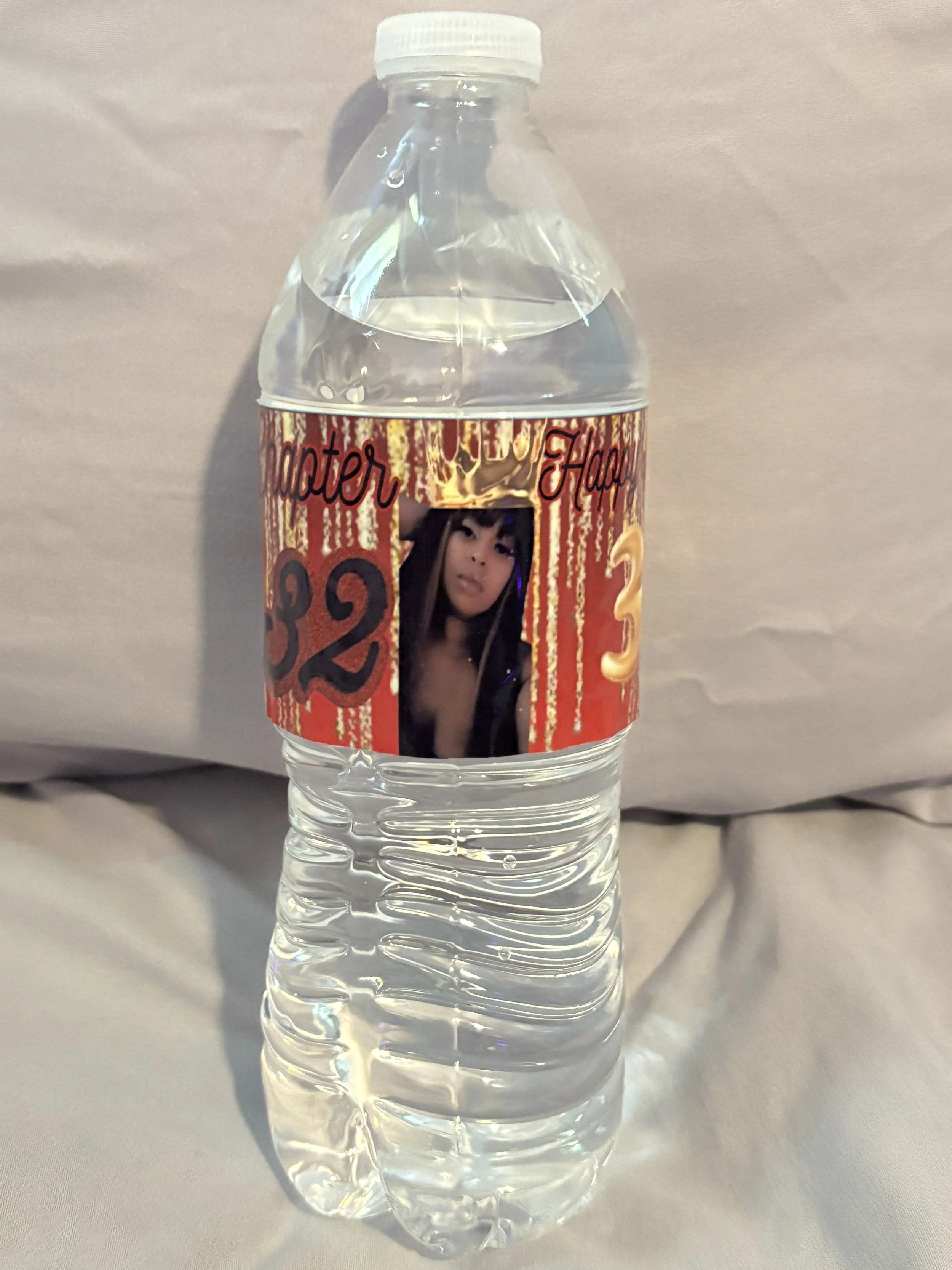 A clear plastic water bottle with a custom label featuring a woman with long dark hair, gold and red background, and the word 'Happier' along with numbers and a photo of the woman.