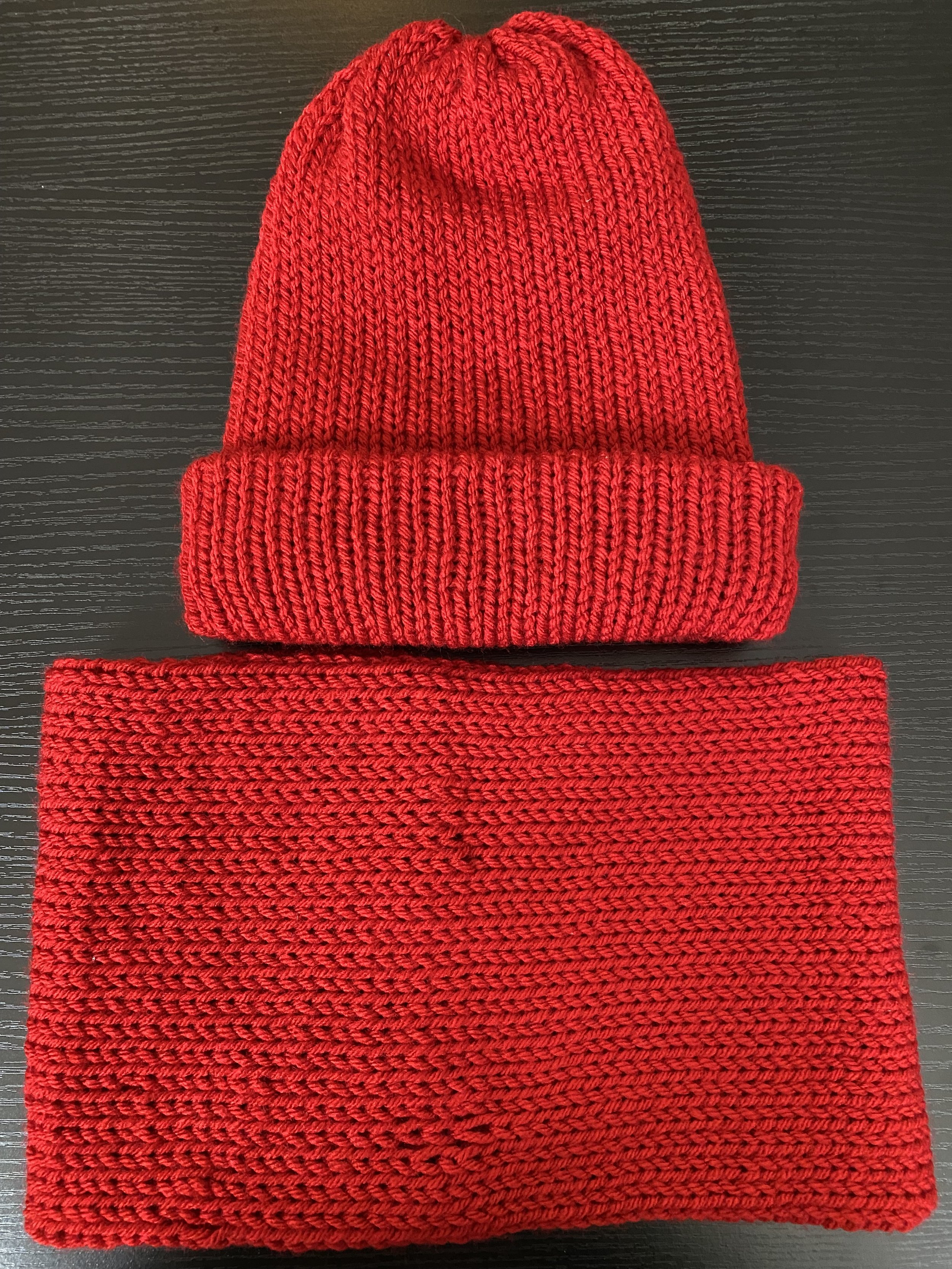 Red knit beanie hat and matching scarf placed on a black surface.