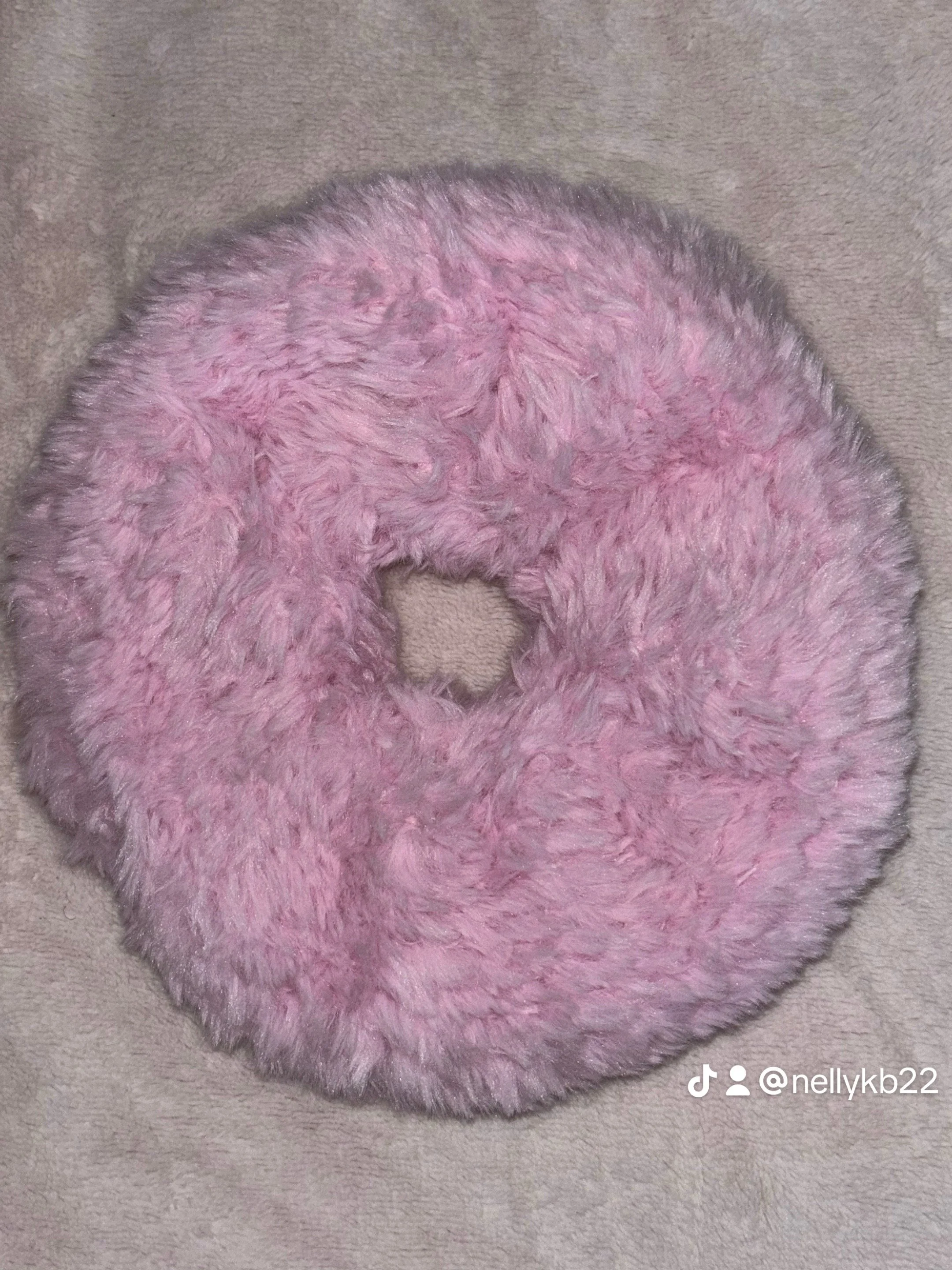 Pink, fluffy, fuzzy donut-shaped object on a beige surface.