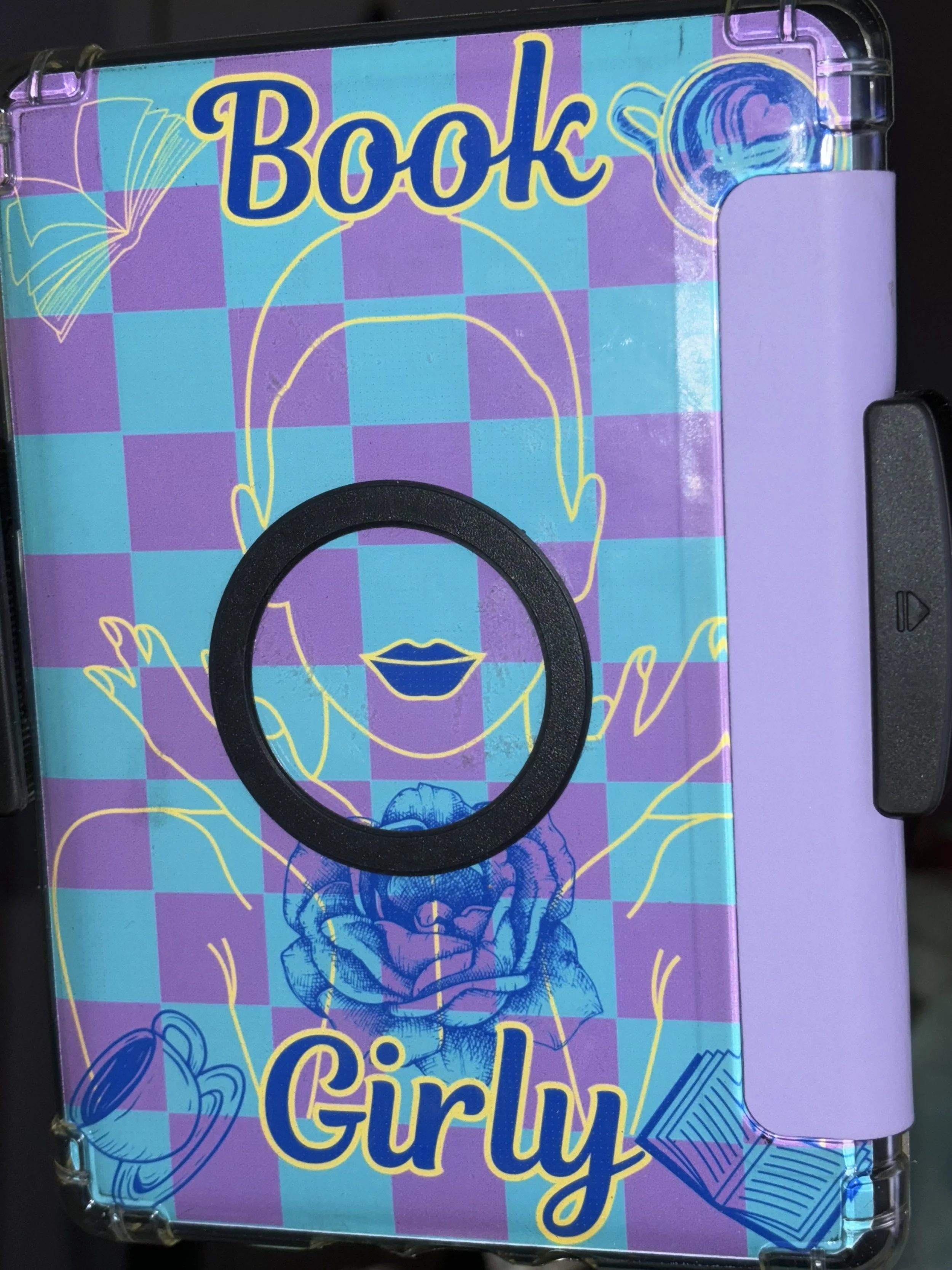 Colorful notebook cover with a checkered purple and teal background, featuring a yellow line drawing of a girl with closed eyes, stylized lips, and a rose on her neck, with the words 'Book Girly' in yellow and blue.