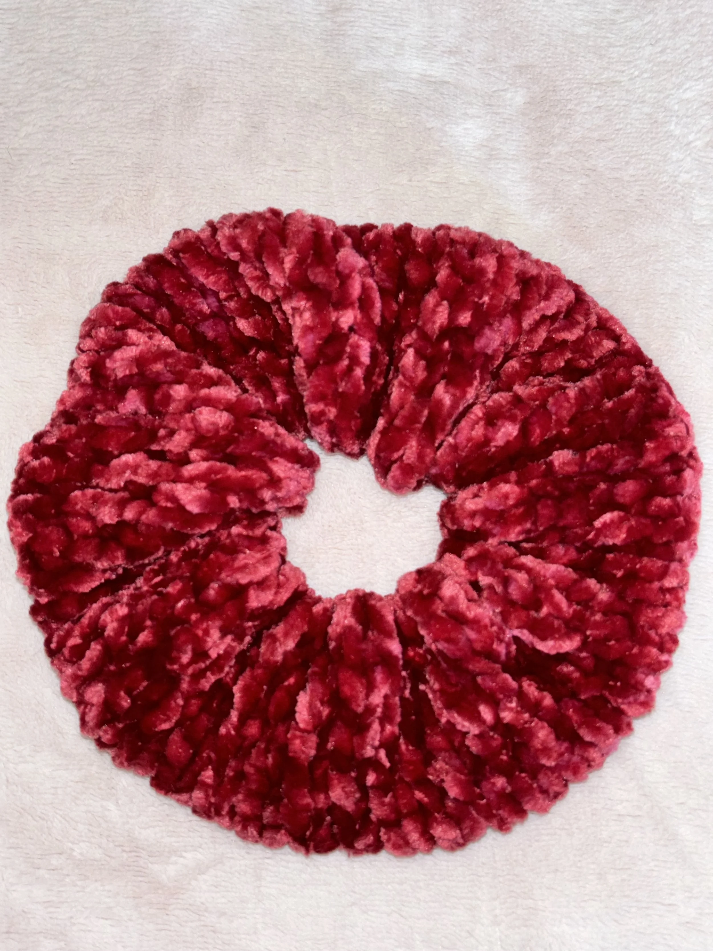 A fluffy, red, circular scrunchie with a ruffled texture on a light-colored background.