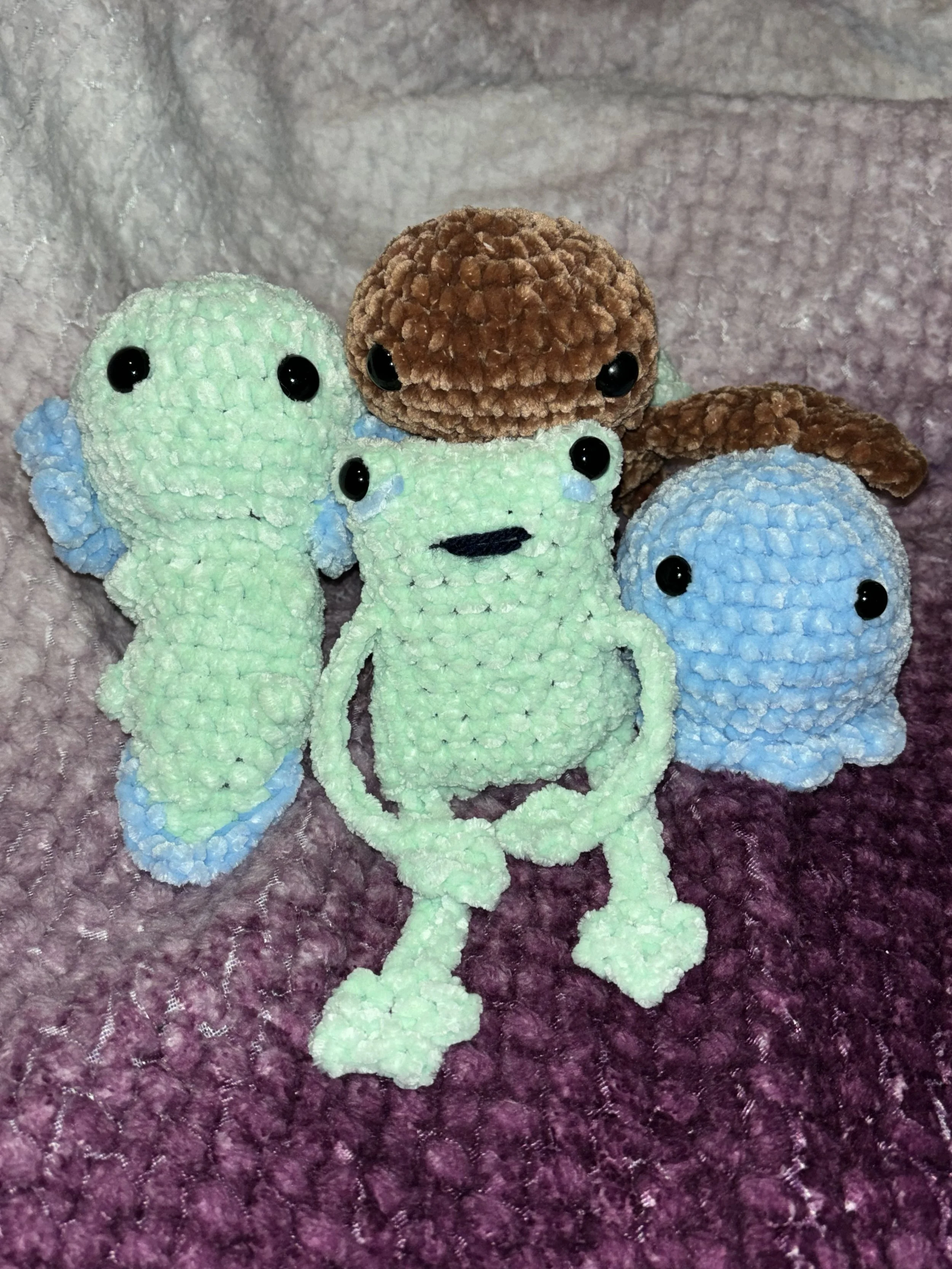 Candied plush toys resembling sea creatures, including light green seahorses, a green fish, and a blue octopus, with two brown plush worms on top, all on a textured purple surface.