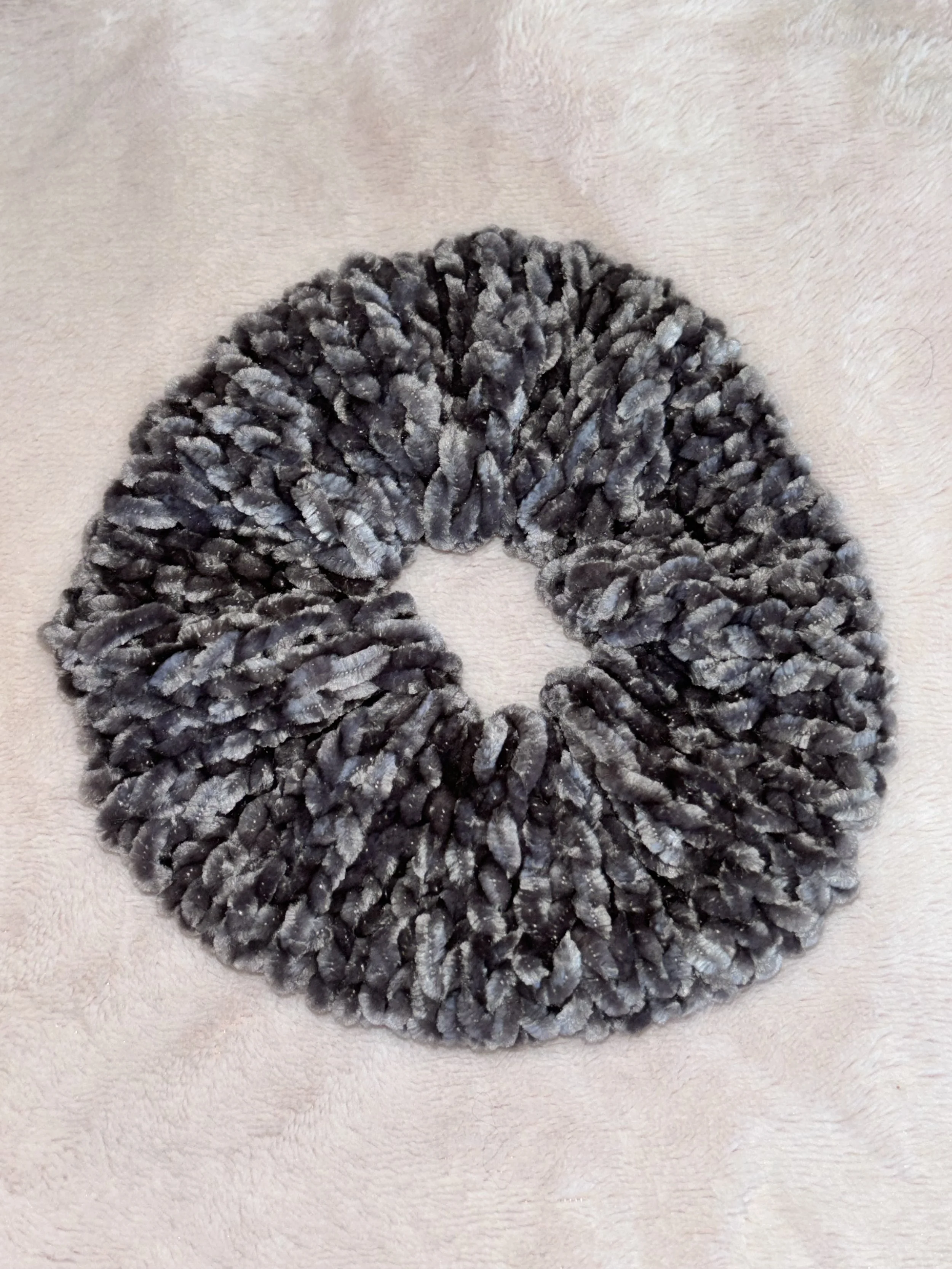 Gray faux fur circular hair scrunchy on a soft pink surface.
