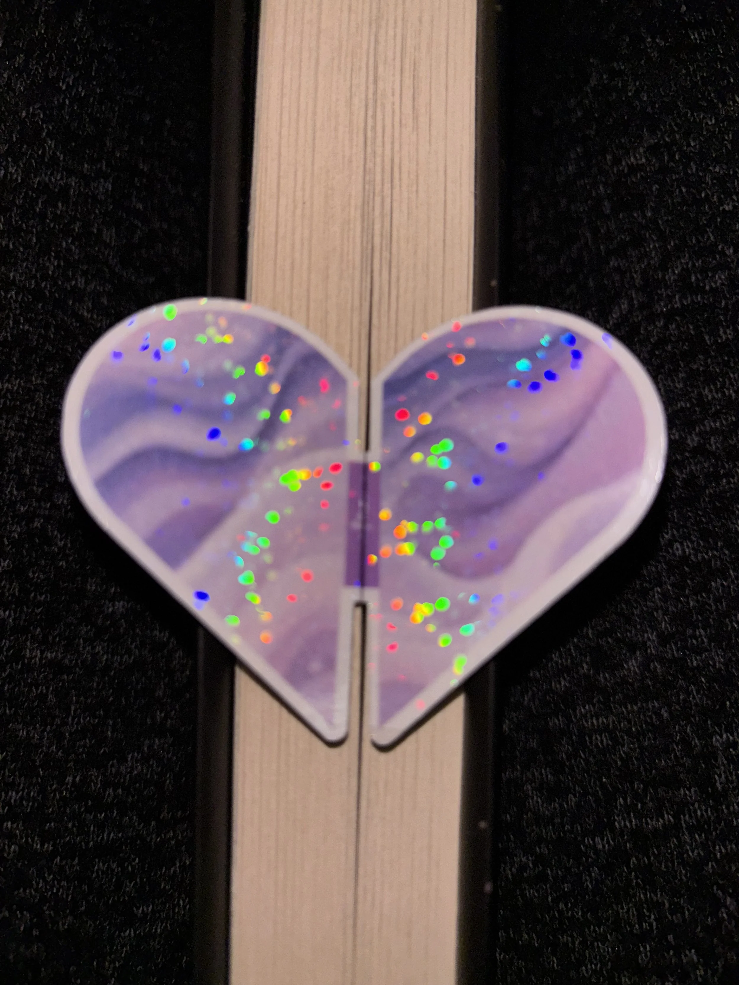 A heart-shaped, holographic sticker with rainbow colors on a wooden surface.