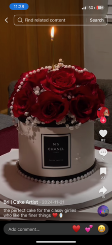 A cake designed to look like a Chanel No. 5 perfume bottle, decorated with red roses, pearl beads, and topped with a lit candle.