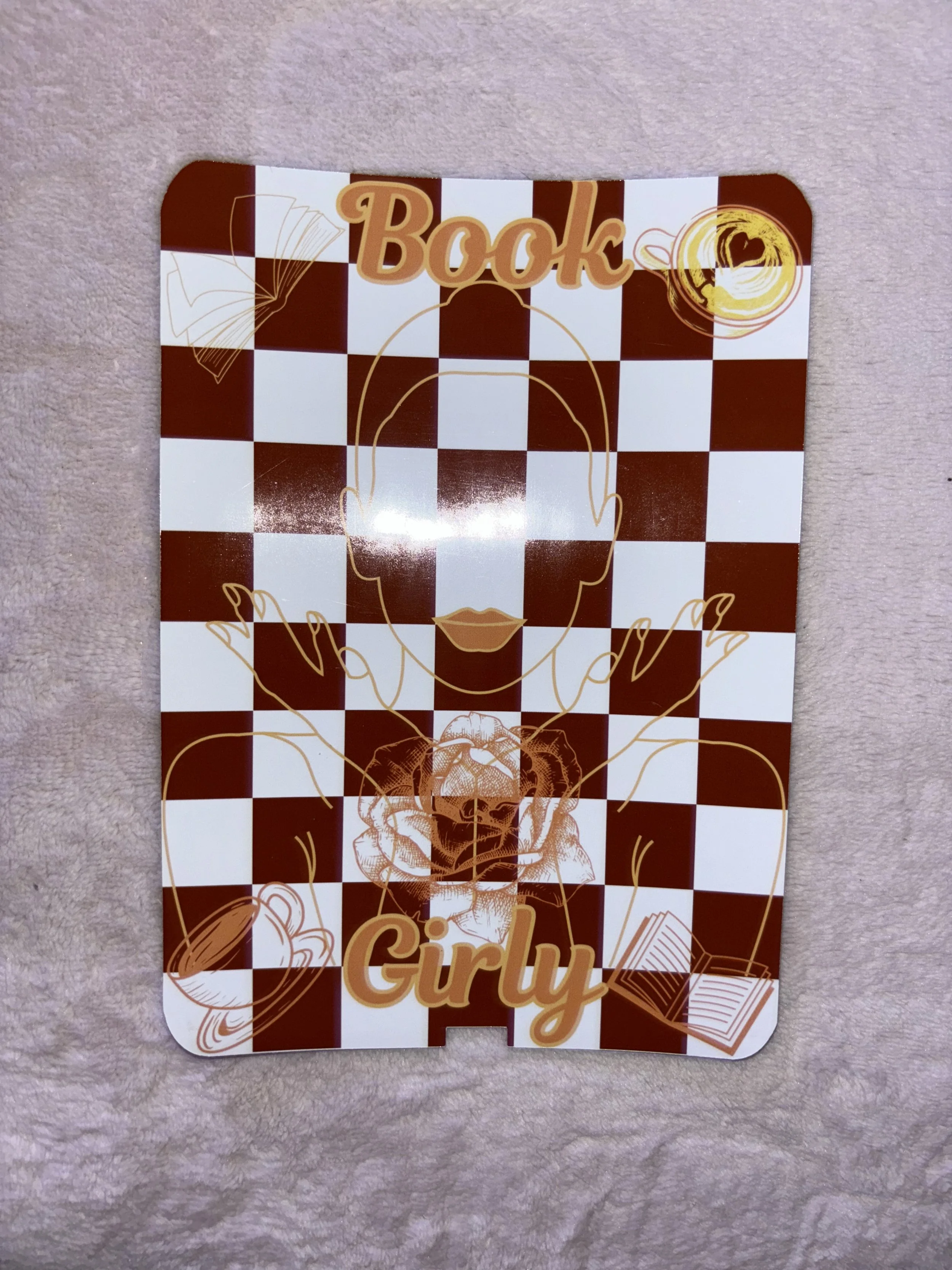 A decorative sign with a red and white checkered background, featuring the words 'Book' at the top and 'Girly' at the bottom, along with line art of a woman's face, a rose, an open book, and a coffee cup.