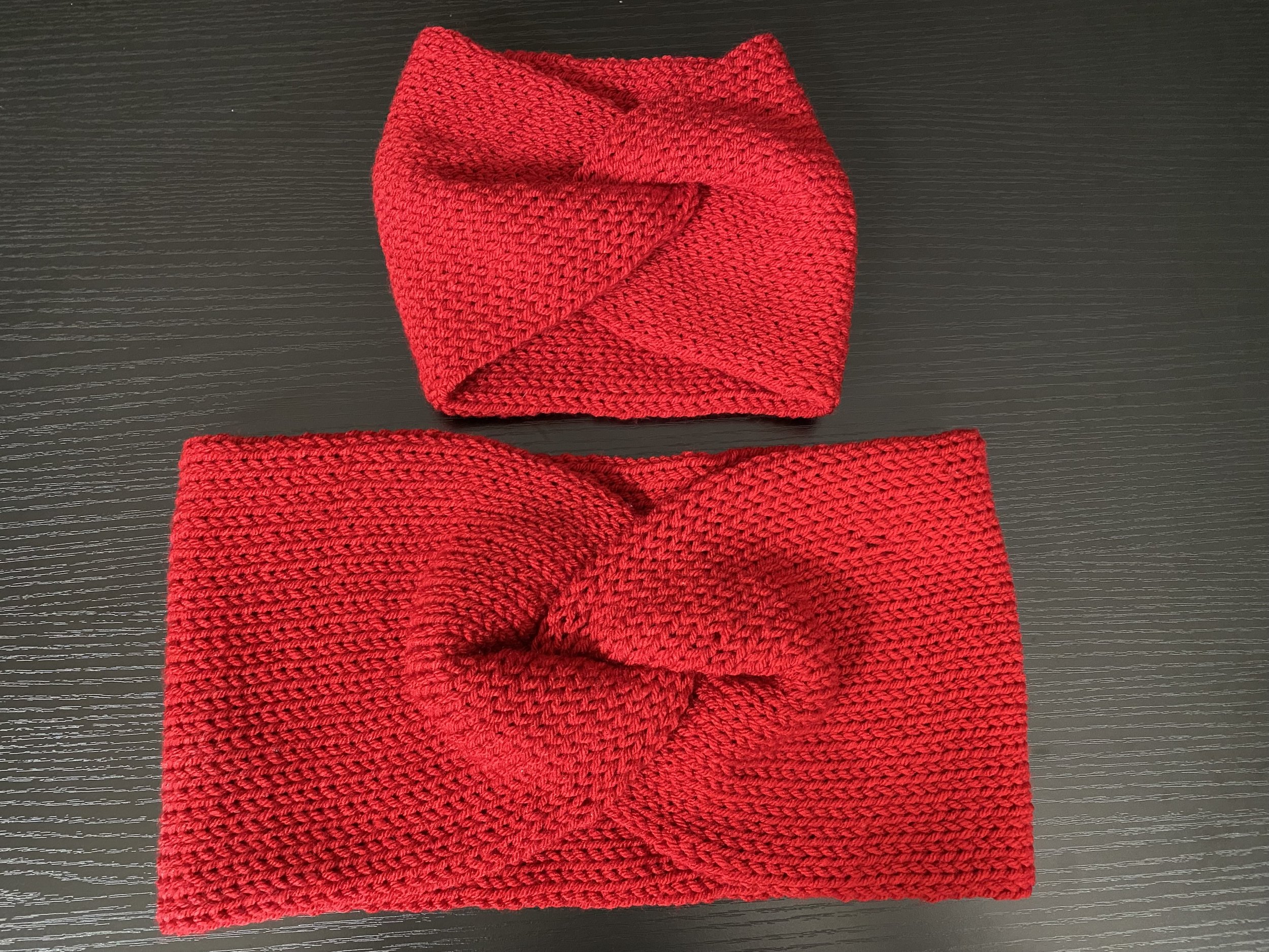 Two red knitted scarves folded in a loop, placed on a black surface.
