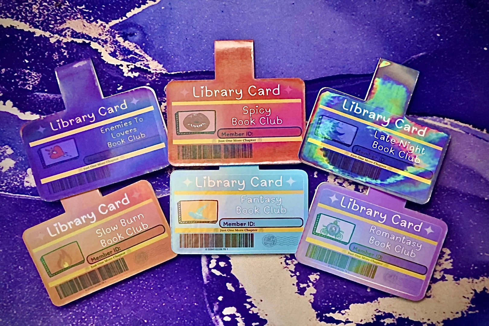 Six colorful library cards, each with unique designs and themed titles, placed on a dark, textured surface.