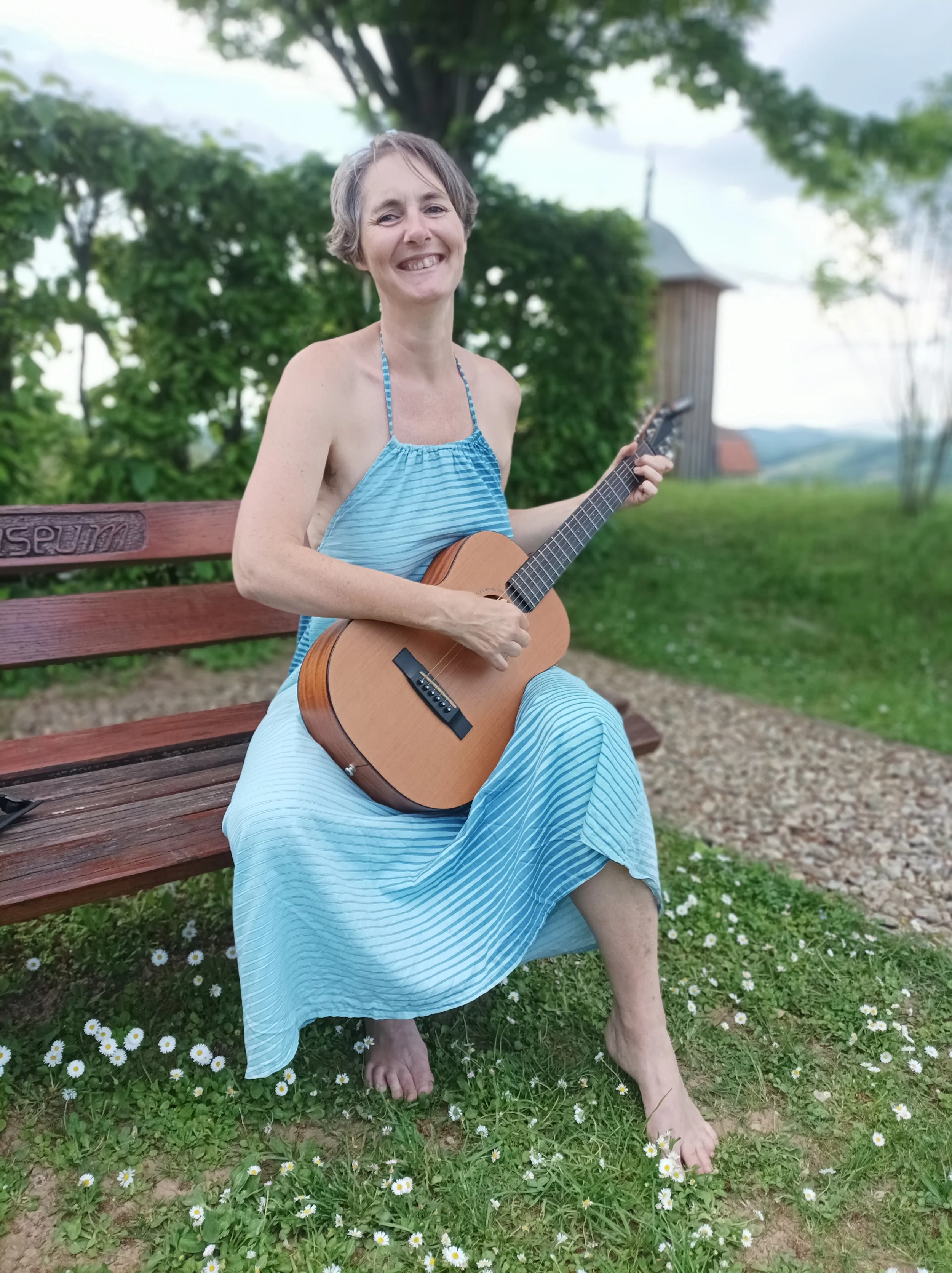 Petra Kasser, sitzt auf einer Bank mit einer Gitarre