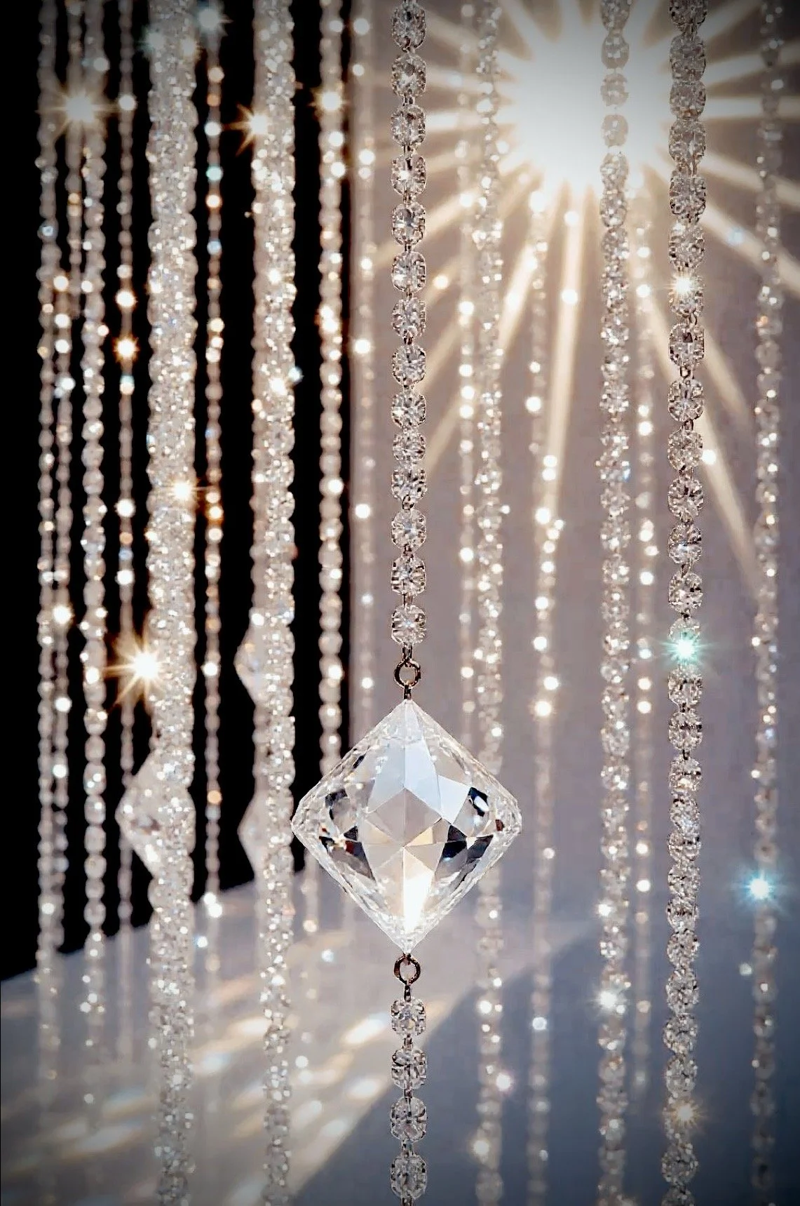 Multiple strands of sparkling crystal beads and a large, multifaceted crystal pendant hanging among them, with sunlight streaming through from behind, creating a shimmering, radiant effect.