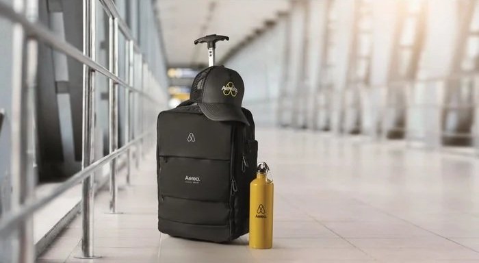 A black backpack with a yellow water bottle and a black hat, sitting on a tiled floor in an airport terminal.