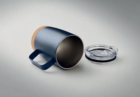 A black ceramic mug lying on its side with a wooden handle next to an empty glass ashtray on a light gray surface.