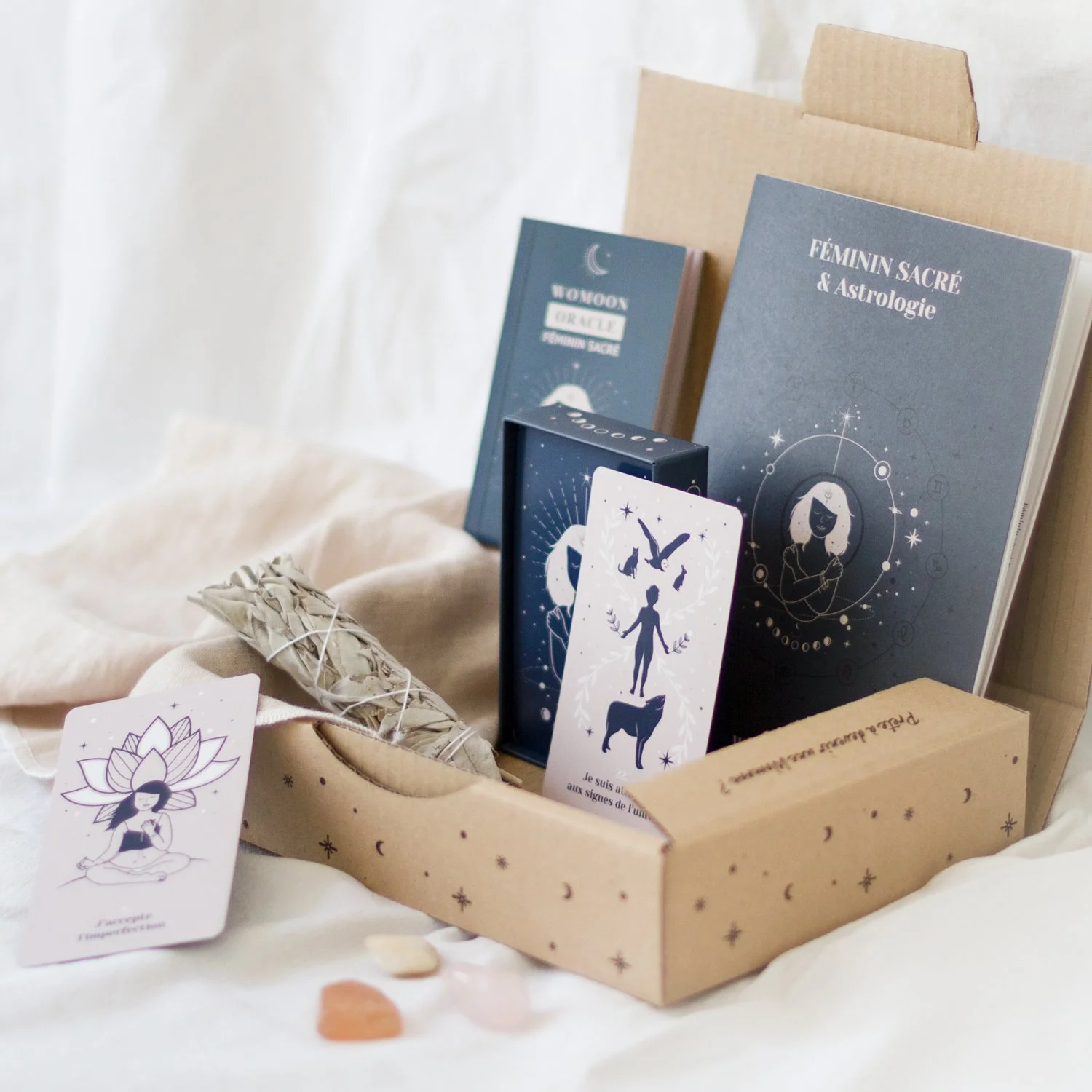 Une boîte en carton contient des cartes de tarot, un bâton de sauge, et des livres sur l'astrologie et la féminité sacrée. Il y a aussi des cristaux. La scène est décorée de petites étoiles et de lunes.
