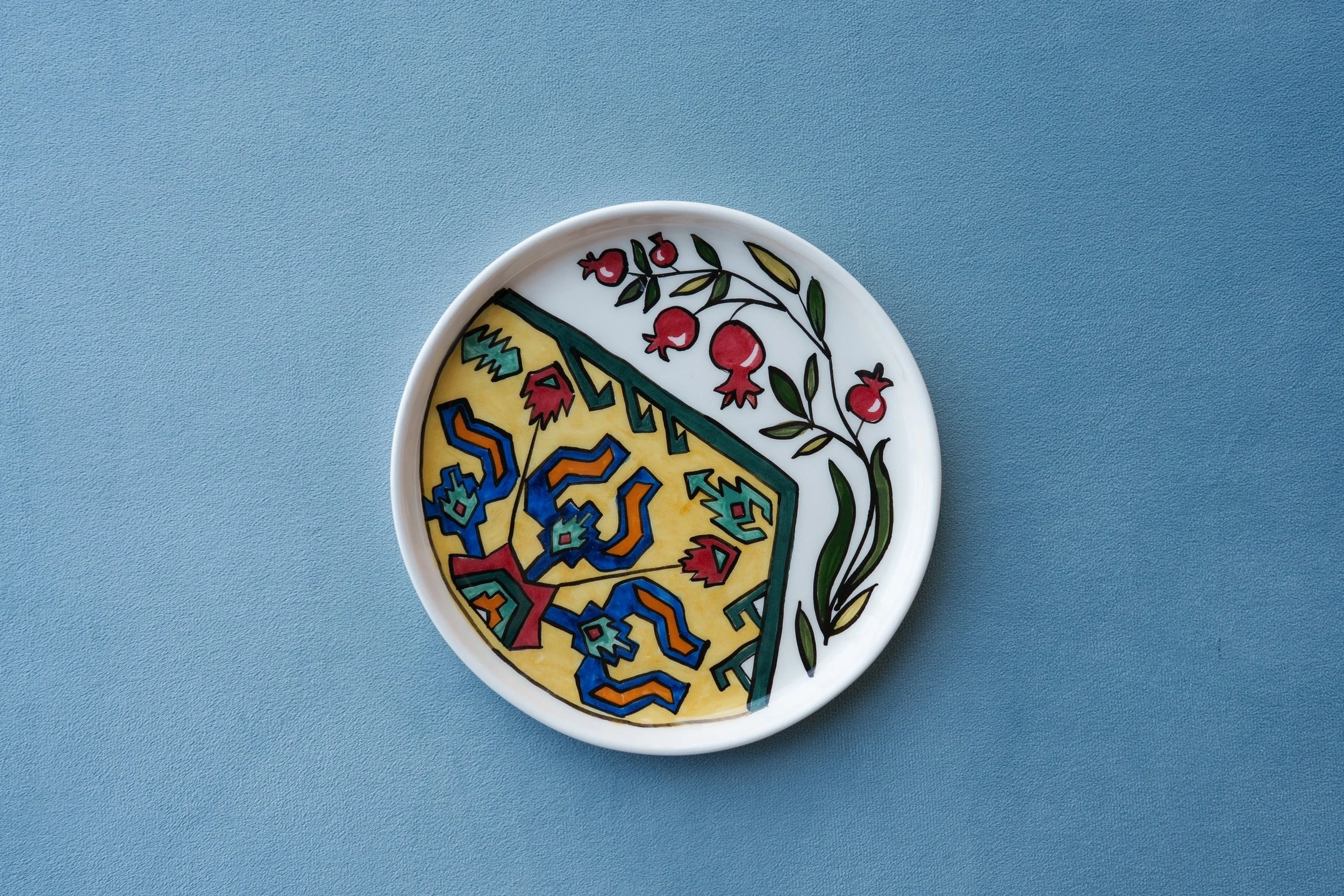 Decorative round ceramic dish with a colorful geometric pattern and a floral design, placed on a blue surface.