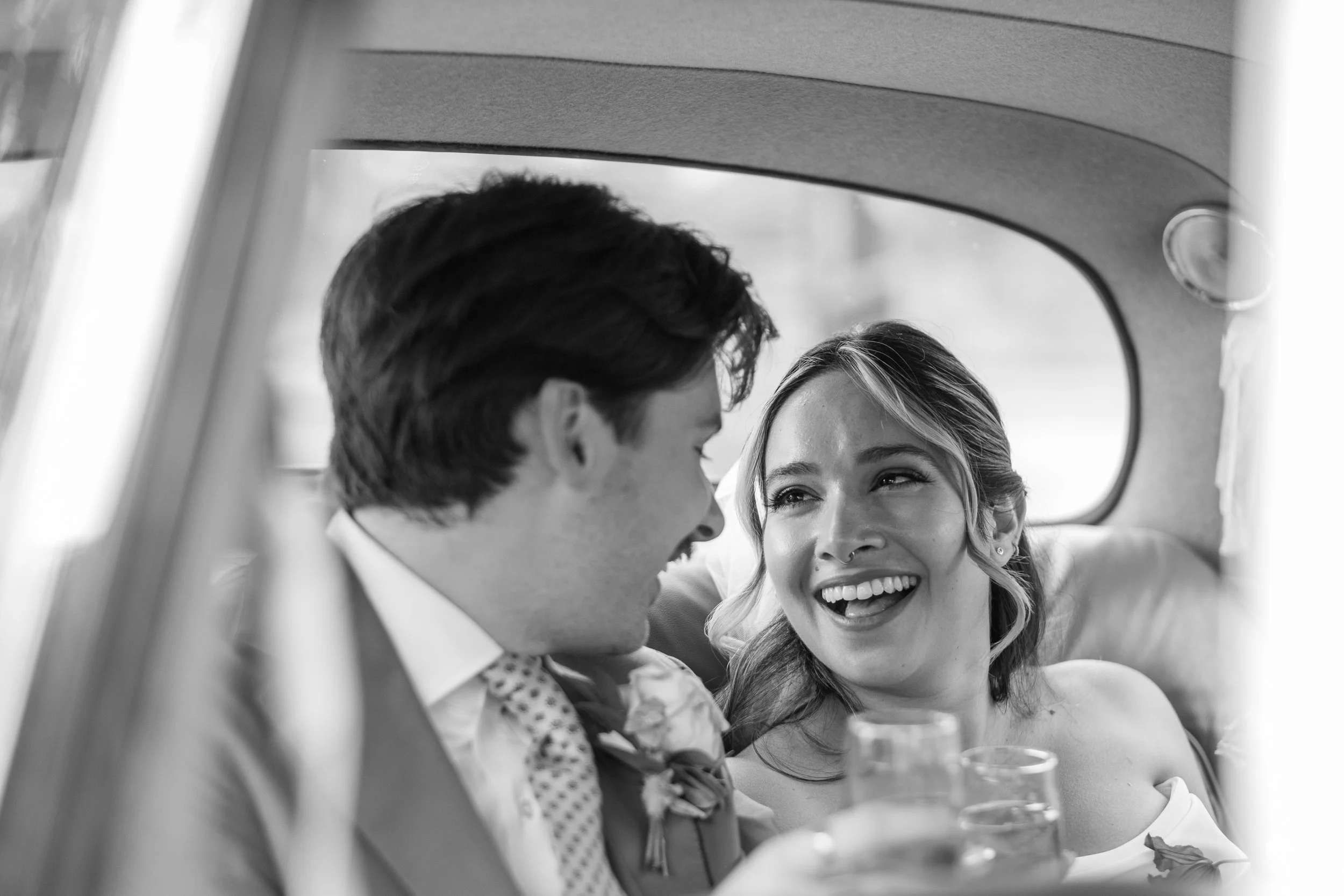 A black and white photo of a smiling woman and man inside a vehicle, sharing a joyful moment.