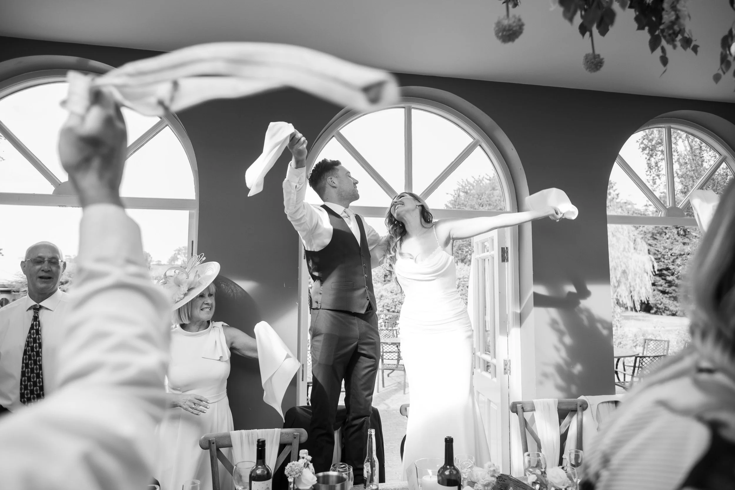A bride and groom dancing joyfully at their wedding reception, with guests around them clapping and celebrating.