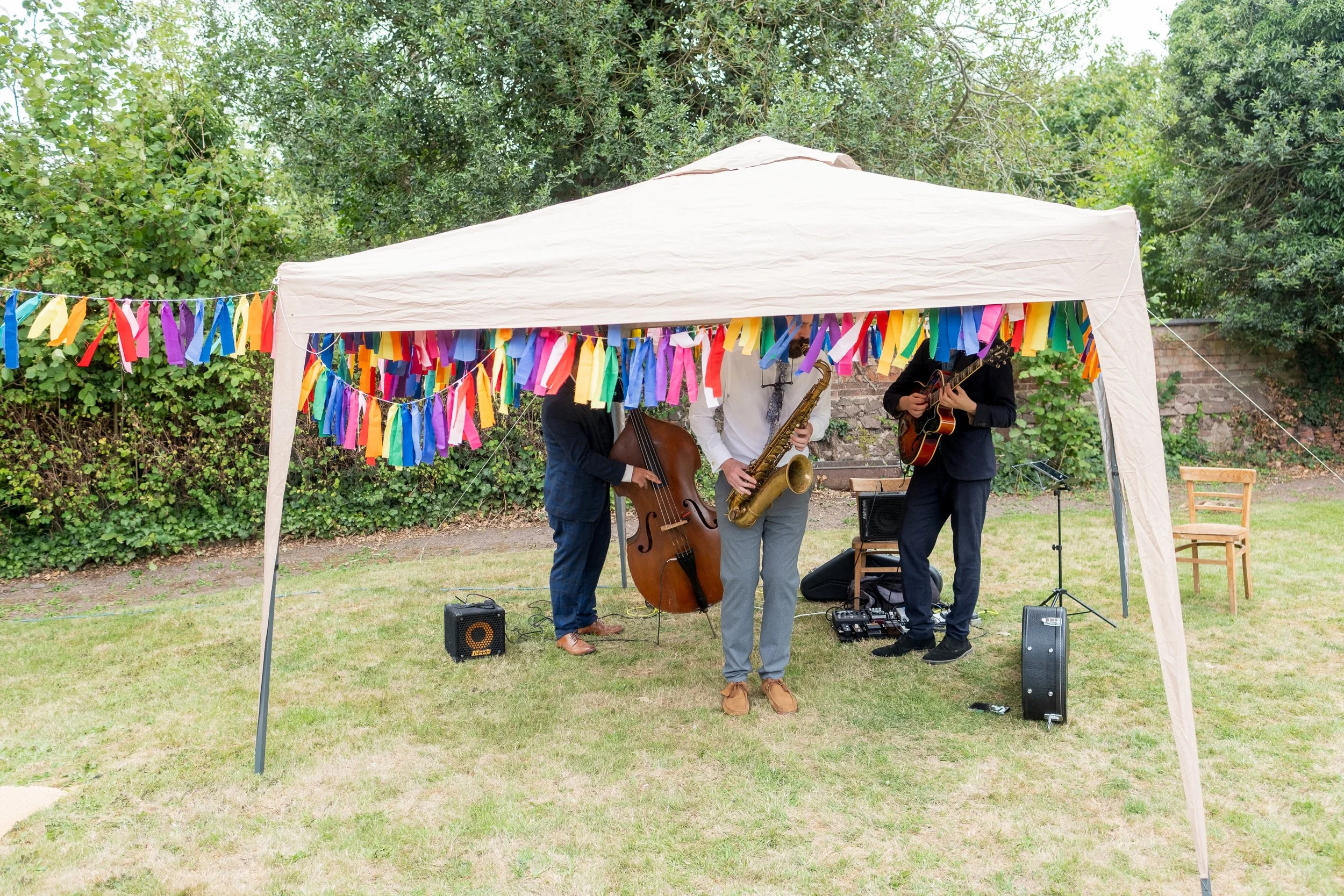 Musicians playing instruments at an outdoor event under a white canopy decorated with colorful ribbons.