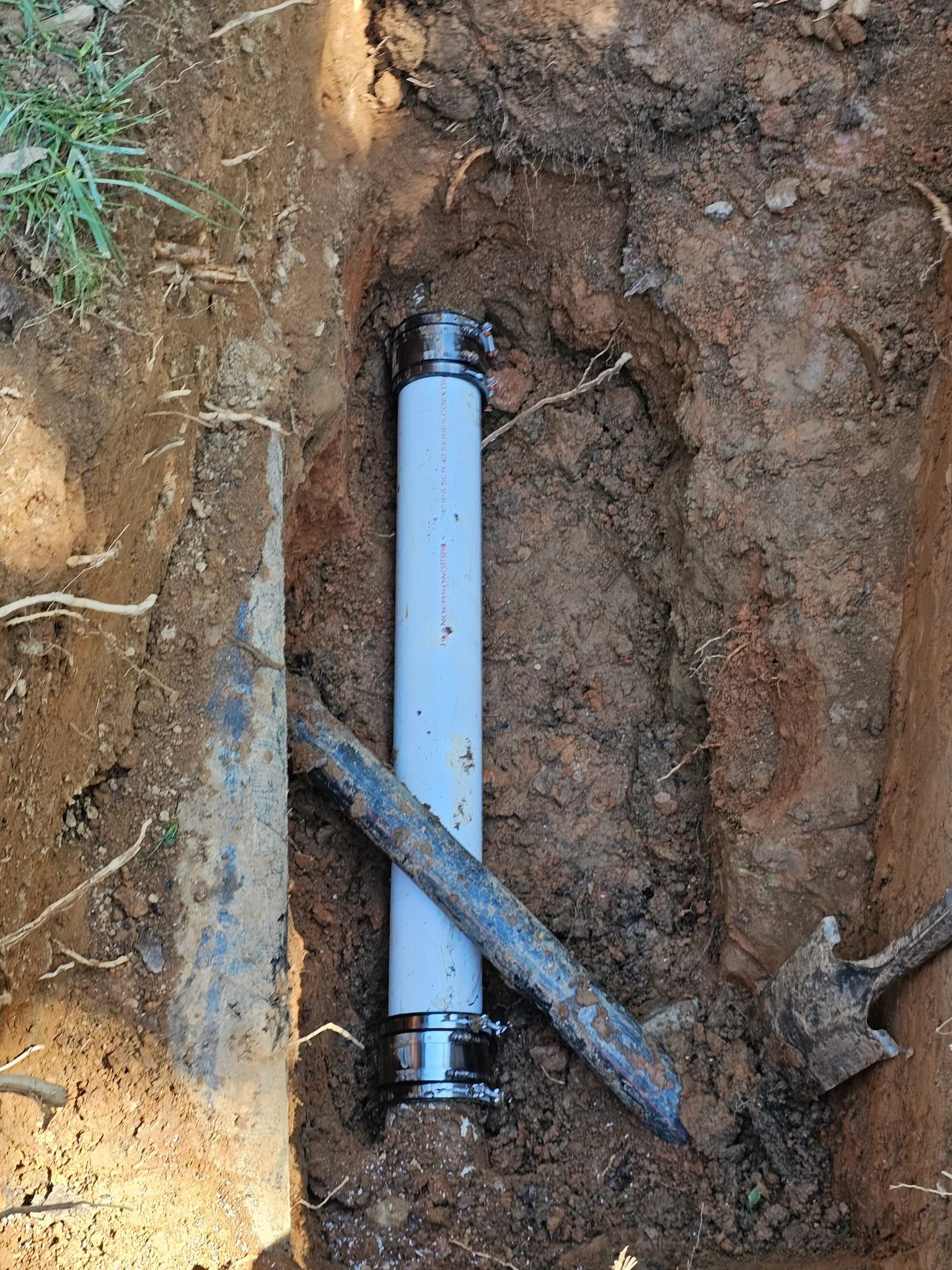 Newly installed underground pipe with black fittings in a trench with dirt and soil surrounding it.