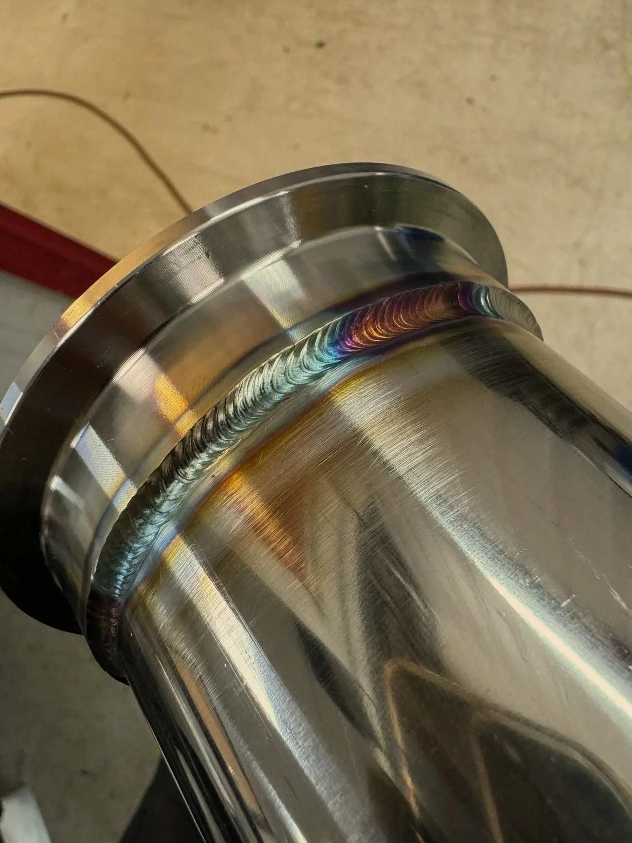 Close-up of a stainless steel pipe with a welded joint showing colorful heat discoloration.