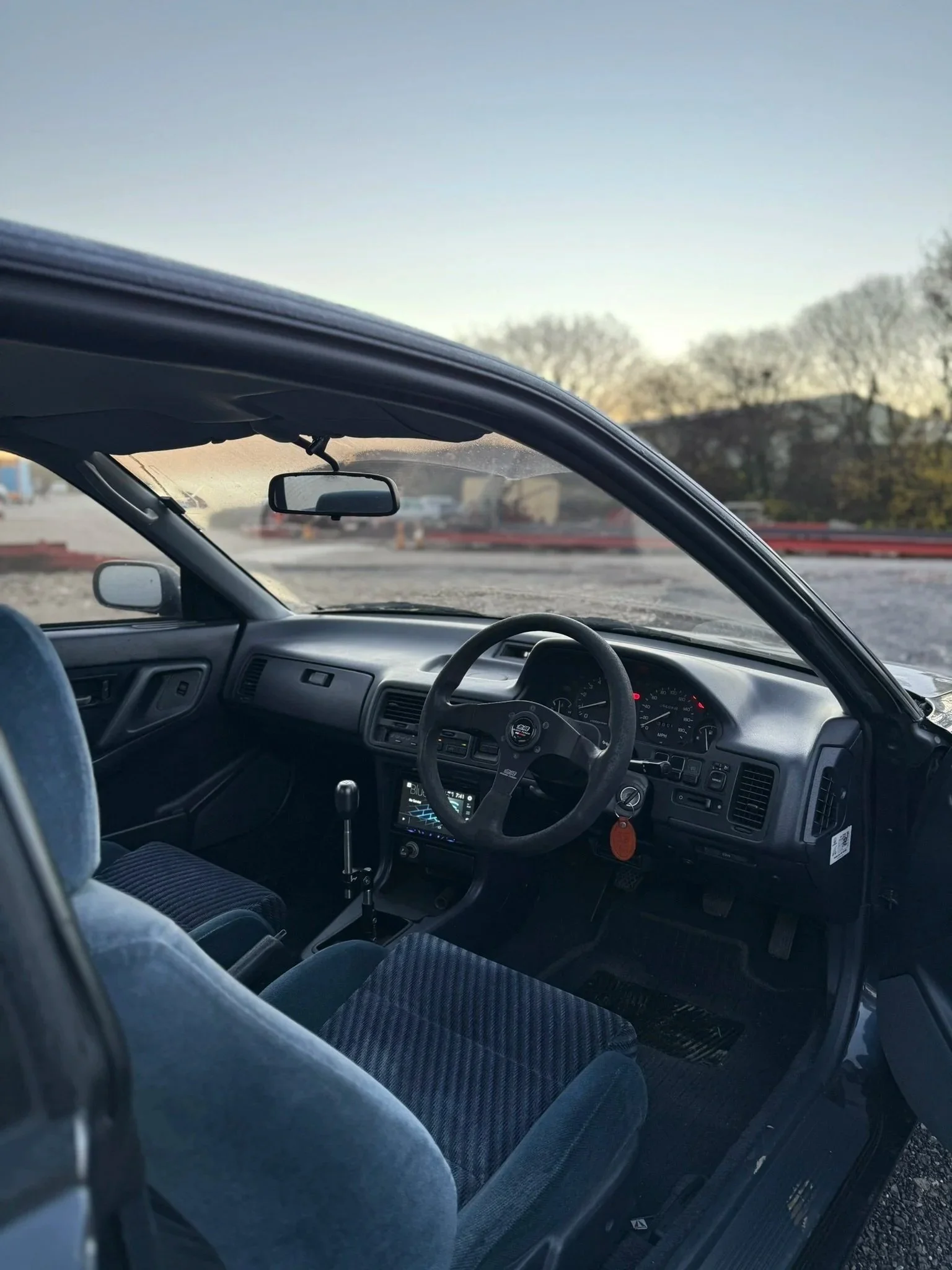 Interior of a car showing the dashboard, steering wheel, gear shift, and front seats with a view of the outside landscape.