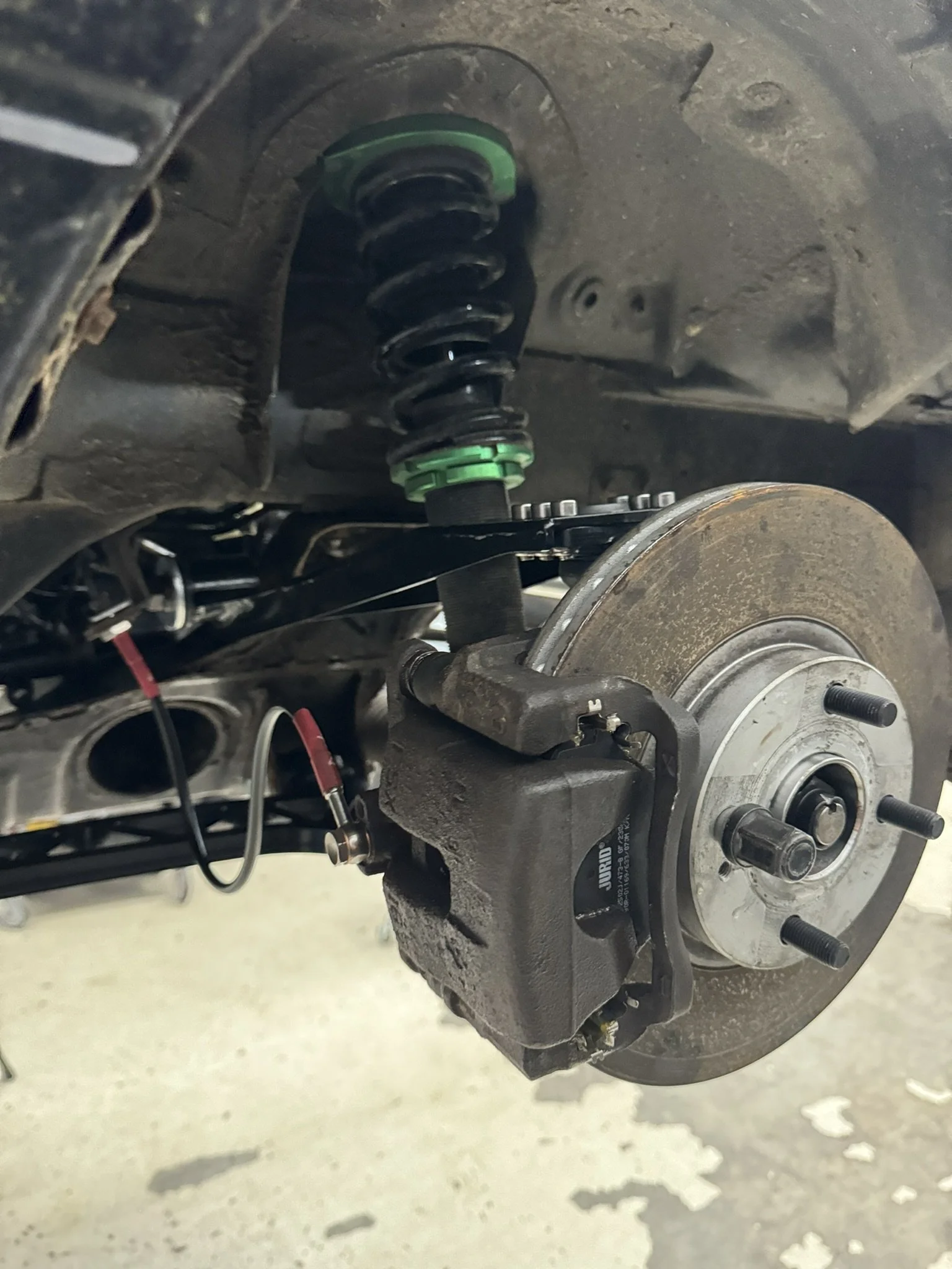 Mazda mx5 A car's front brake assembly and suspension system, including a brake caliper, rotor, and coil spring.