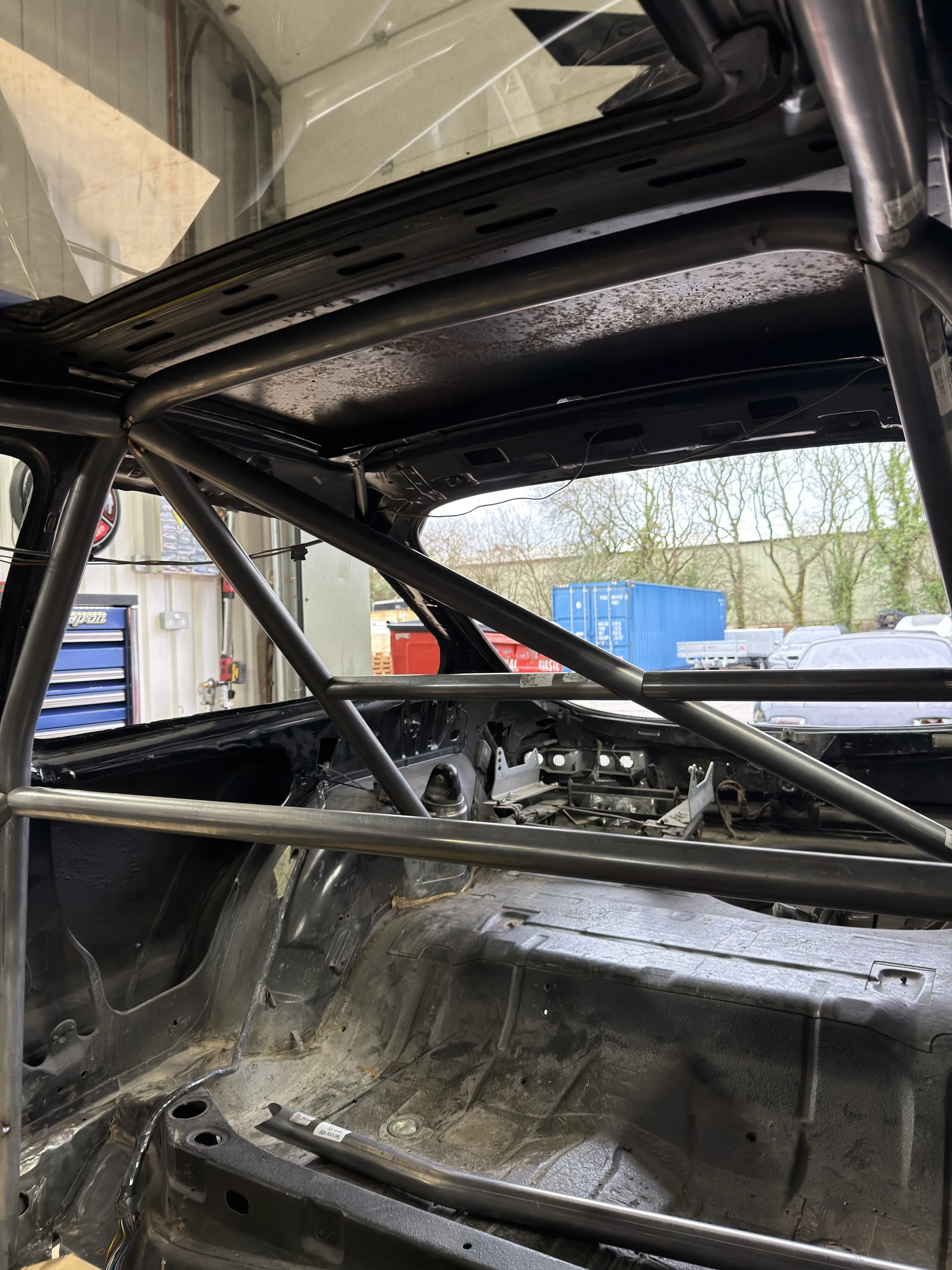 Interior of a race car with a black roll cage and stripped-down interior, showing no seats or dashboard FORD SEIRRA ROLL CAGE