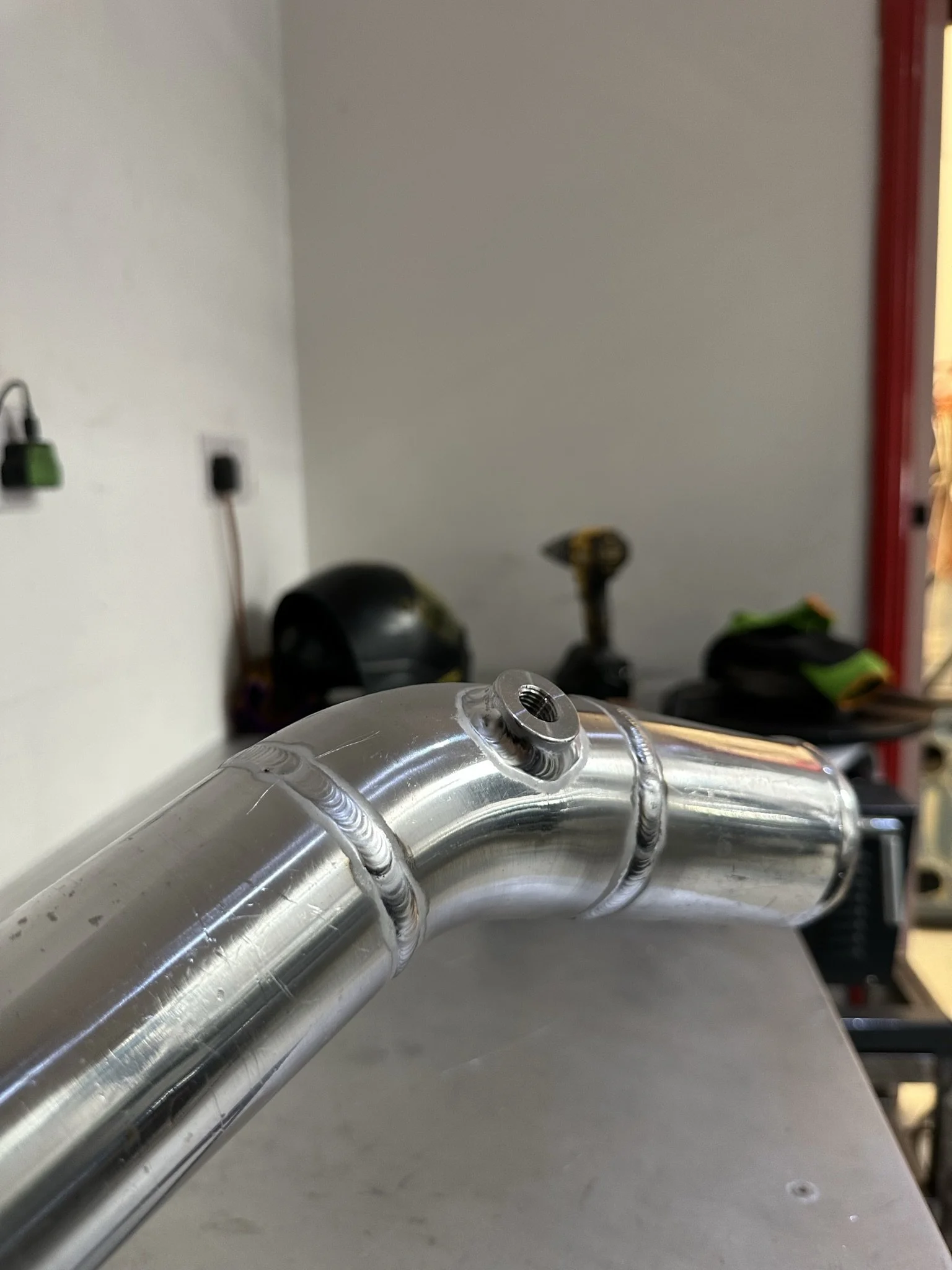 Close-up of a metal pipe with a welded joint and a threaded hole on a workbench in a workshop.