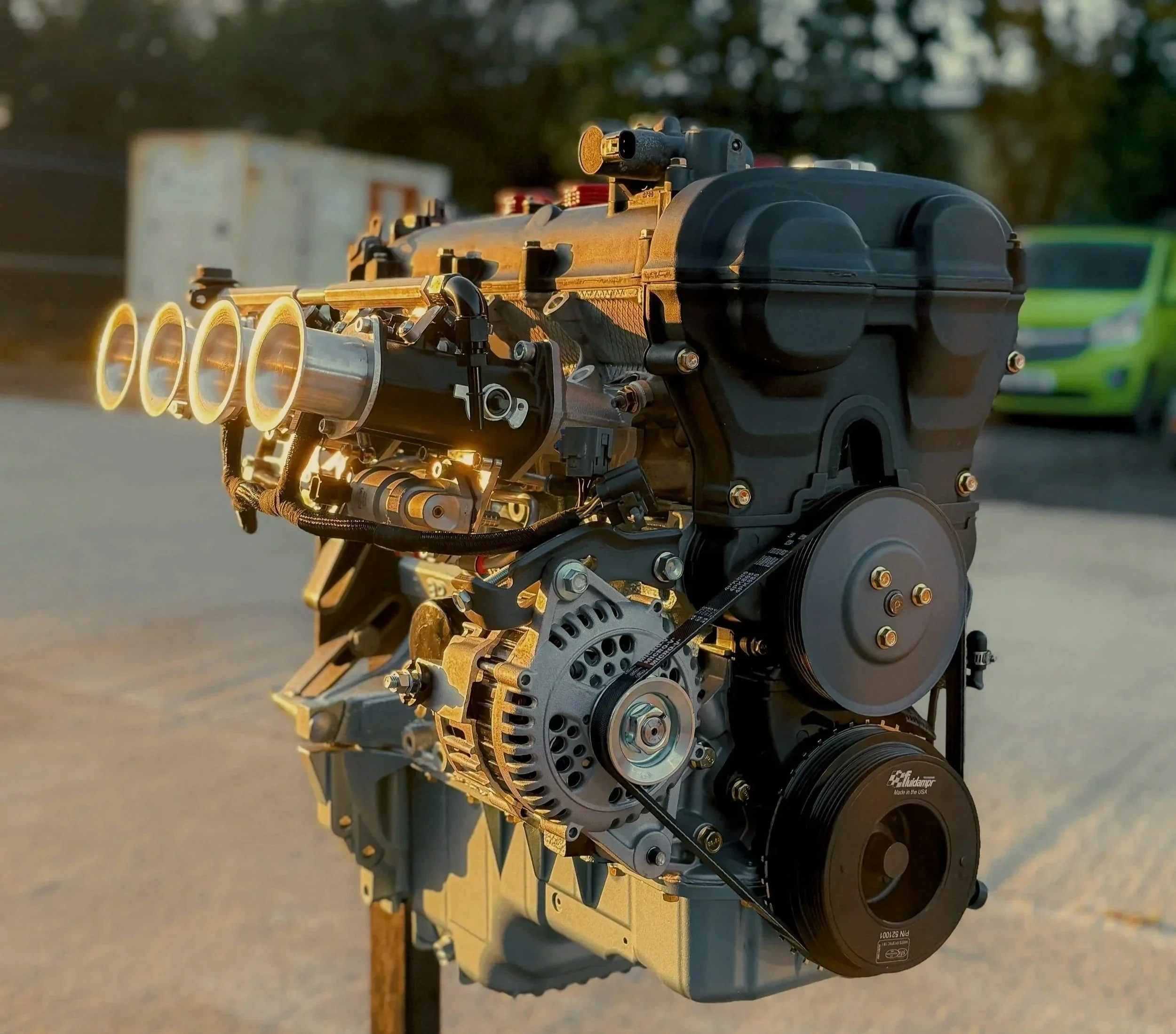 Mazda Mx5 ITB VVT 1.8 A car engine is displayed outdoors with a blurred background of trees and cars, illuminated by sunlight.