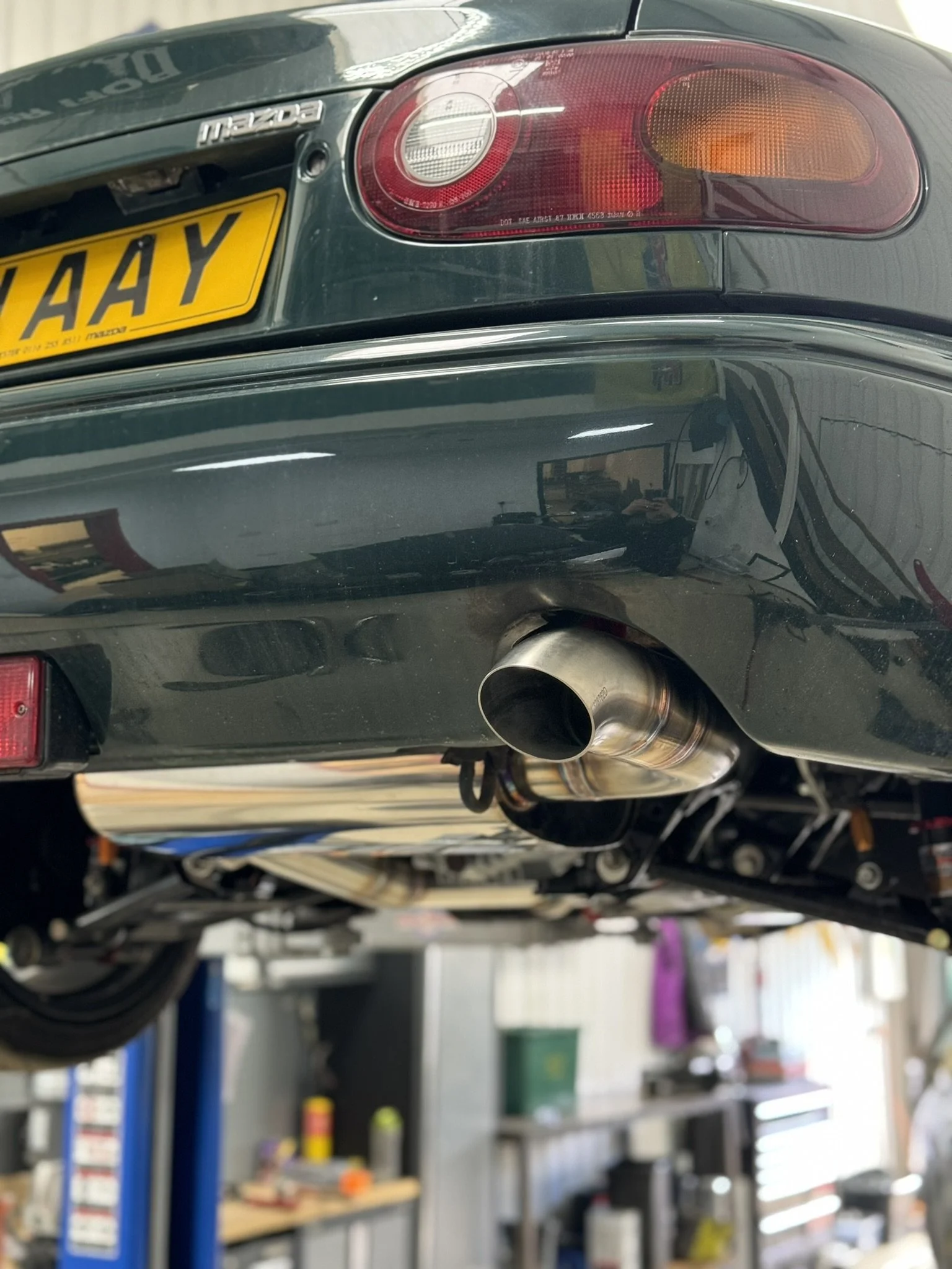 The rear view of a black Mazda car showing the license plate, taillight, and exhaust pipe in a garage or workshop Mazda Miata MX5 MK1 Eunos 