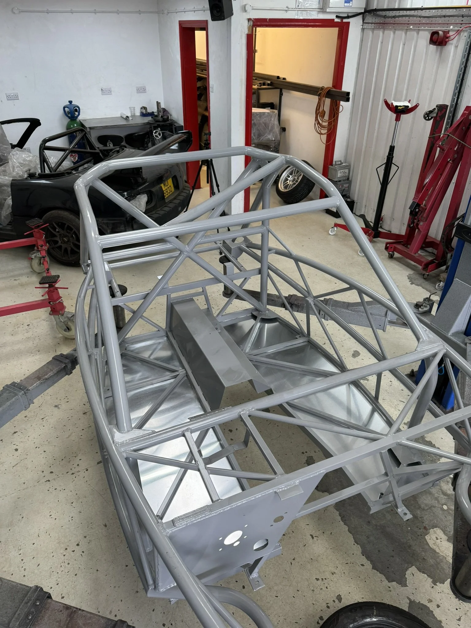 Metal chassis frame of a race car in a workshop with various tools and equipment around.