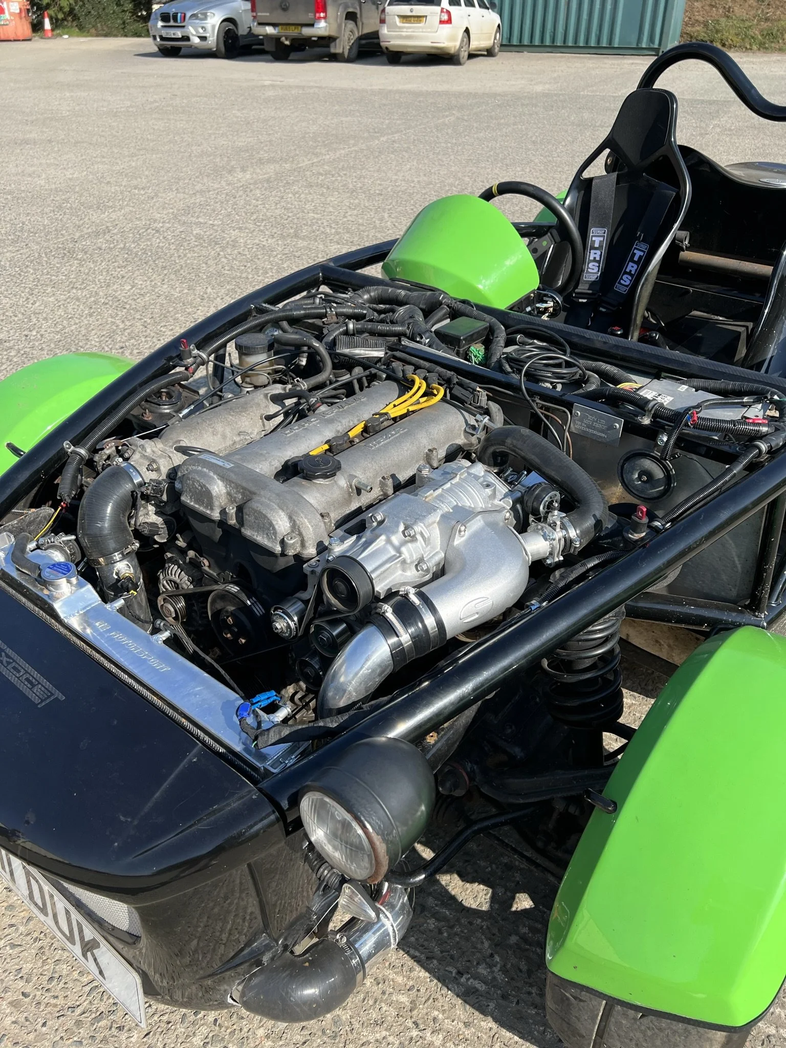 Close-up of the engine bay of a race car with green fenders, showing an exposed engine and various mechanical components.
MEV Exocet