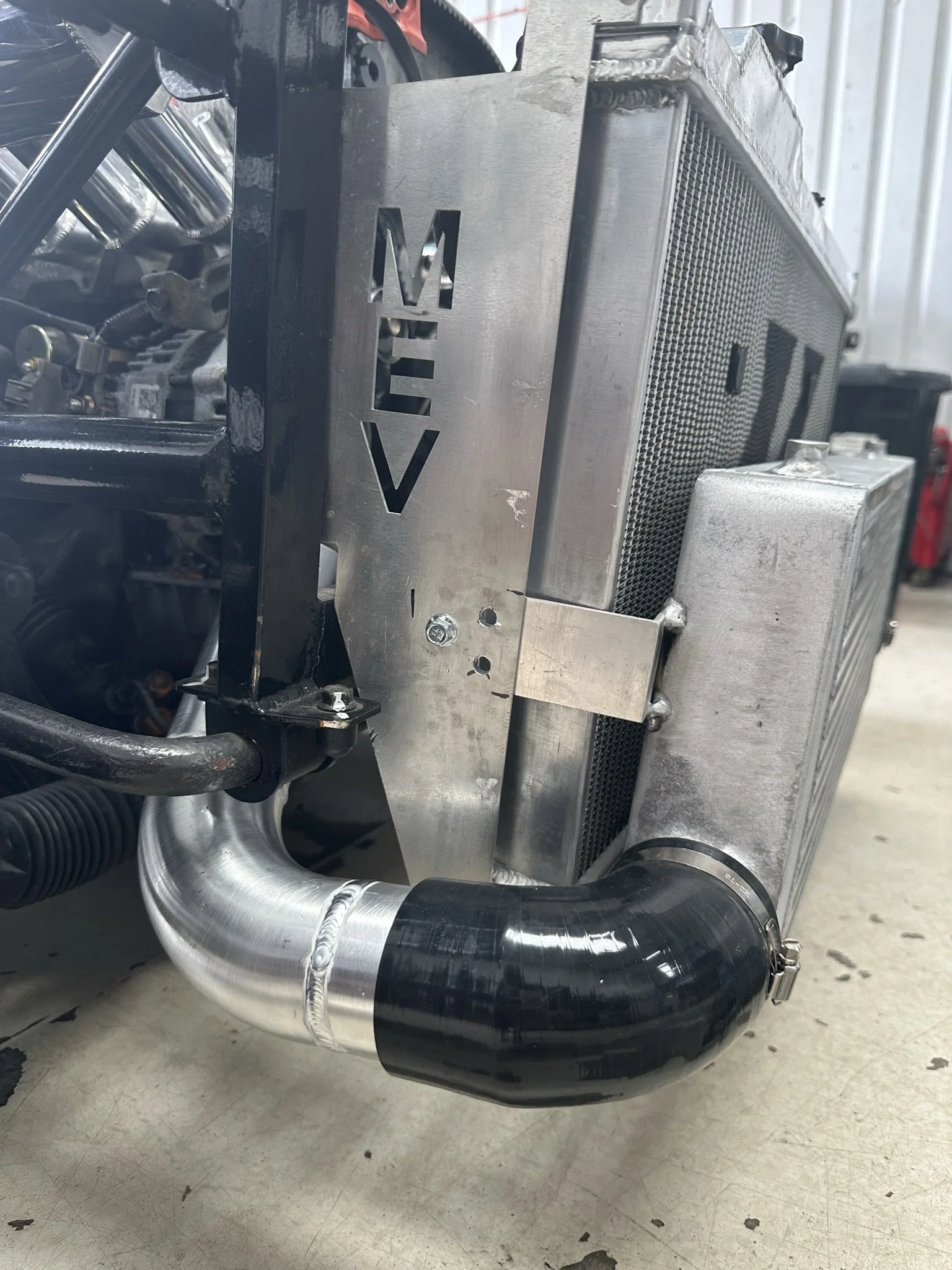 Close-up of a car radiator with a metal support bracket, connected to a tubo with a black silicone hose clamp.