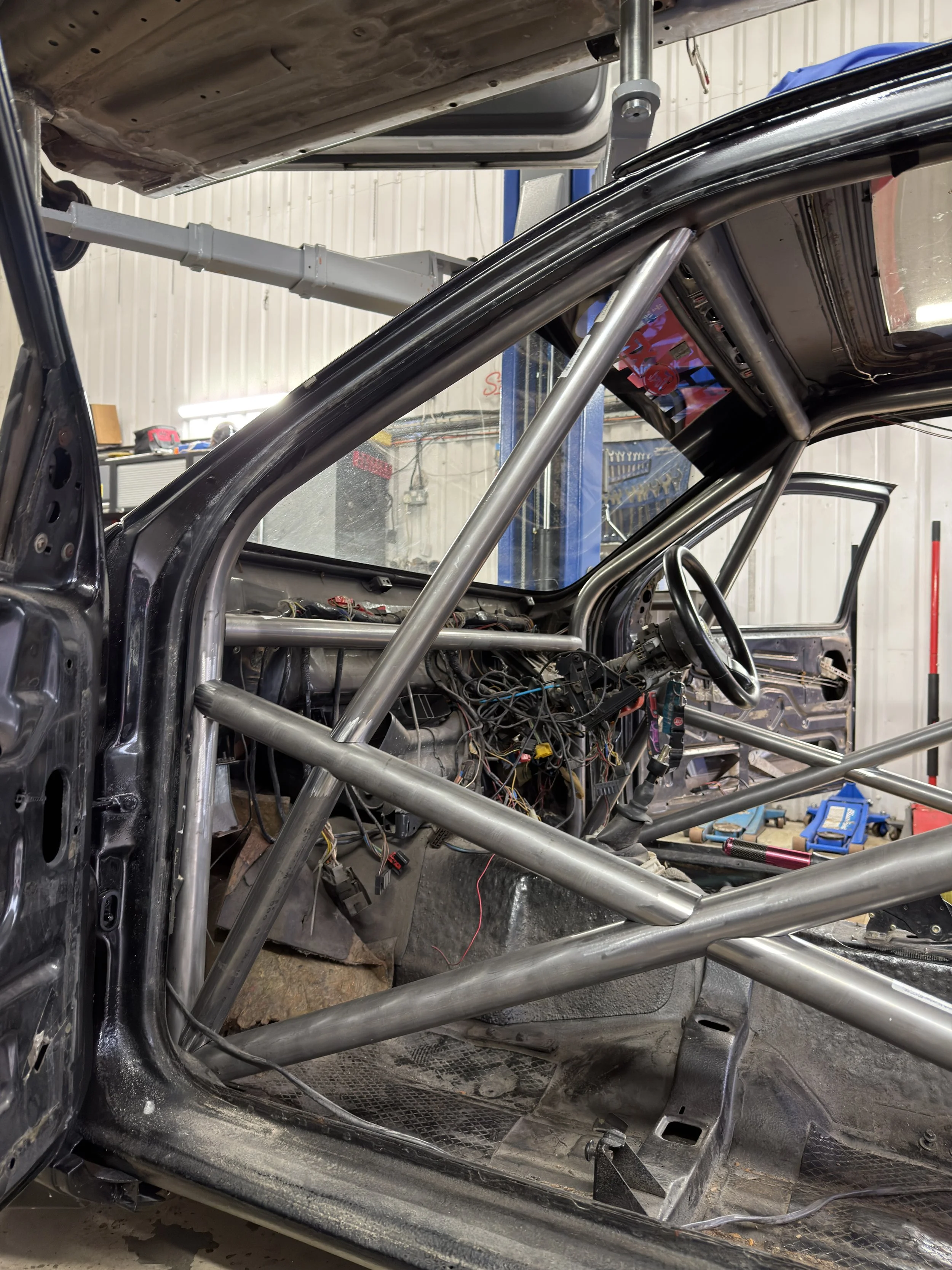 Interior of a race car under construction with a roll cage, dashboard wiring, and no seats. FORD SEIRRA ROLL CAGE