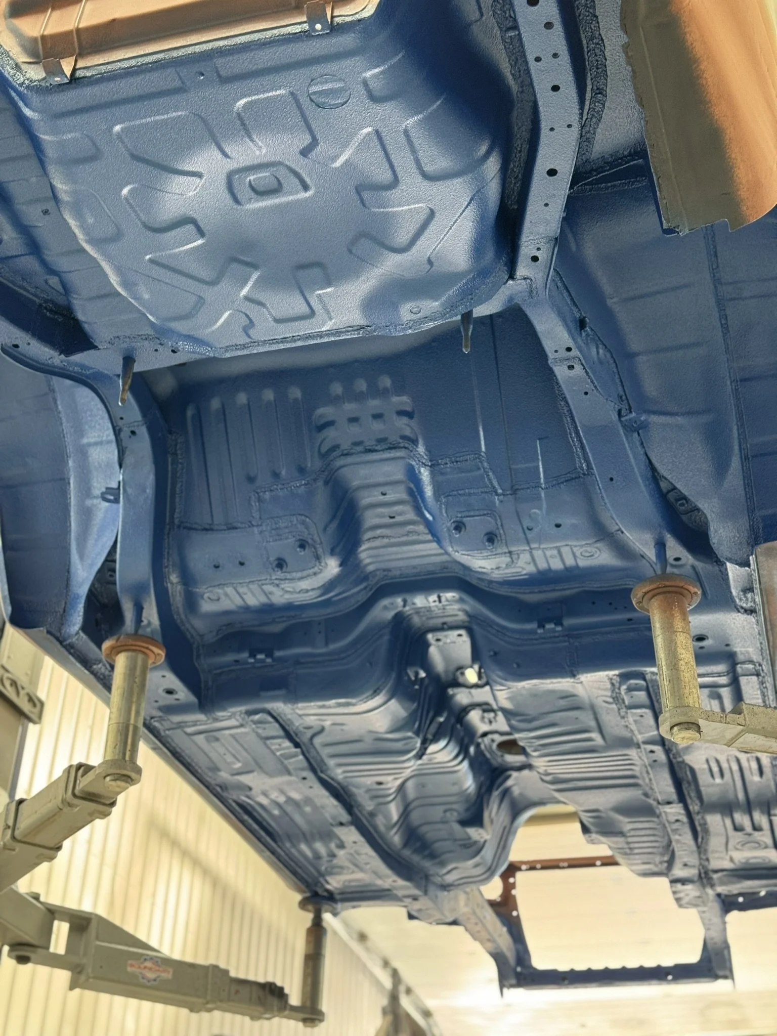 Underside of a car with new blue paint, showing the chassis and structural components, lifted on supports in a workshop. Nissan skyline r33