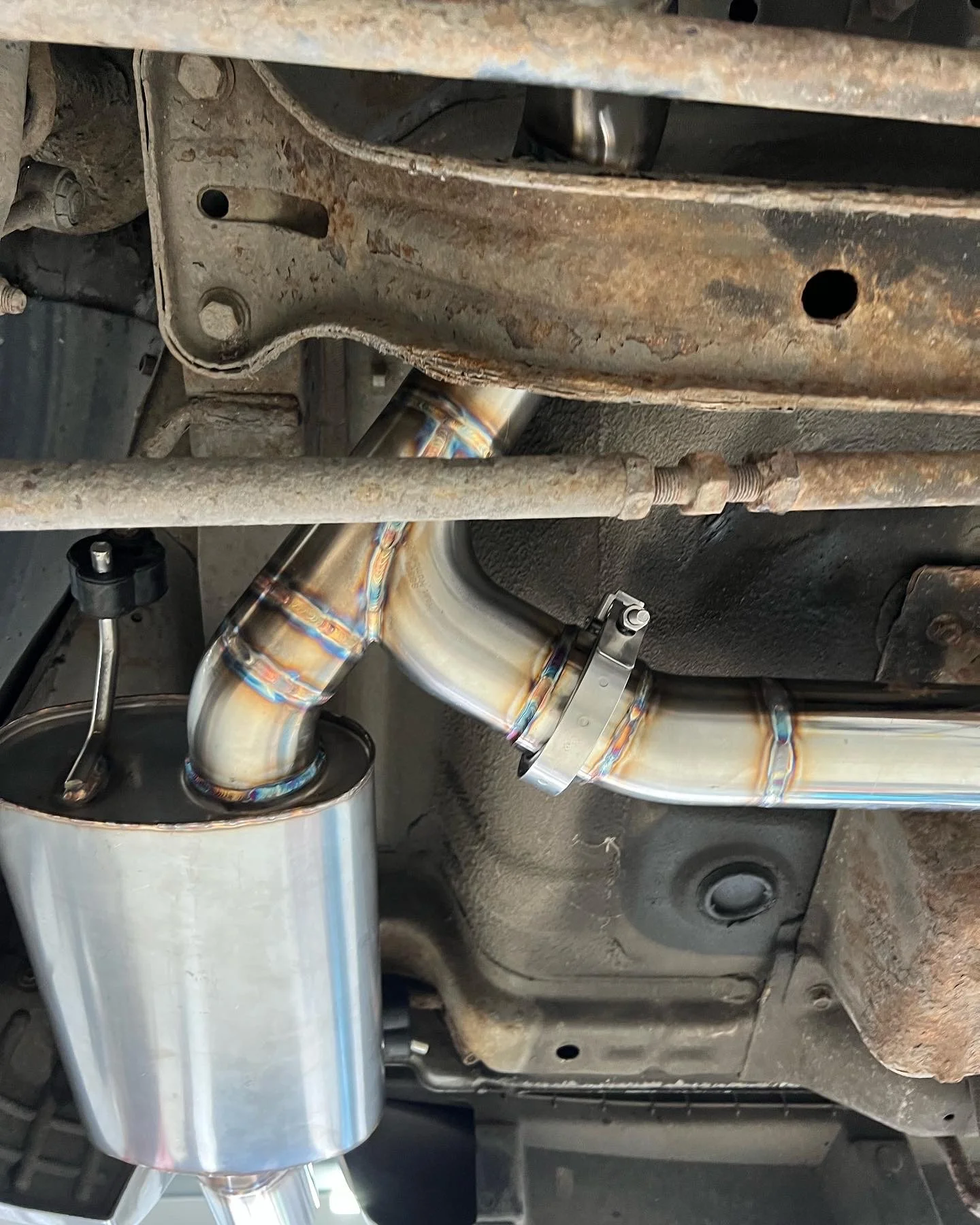Underneath a vehicle showing a shiny aftermarket exhaust system with welded pipe connections and a muffler.