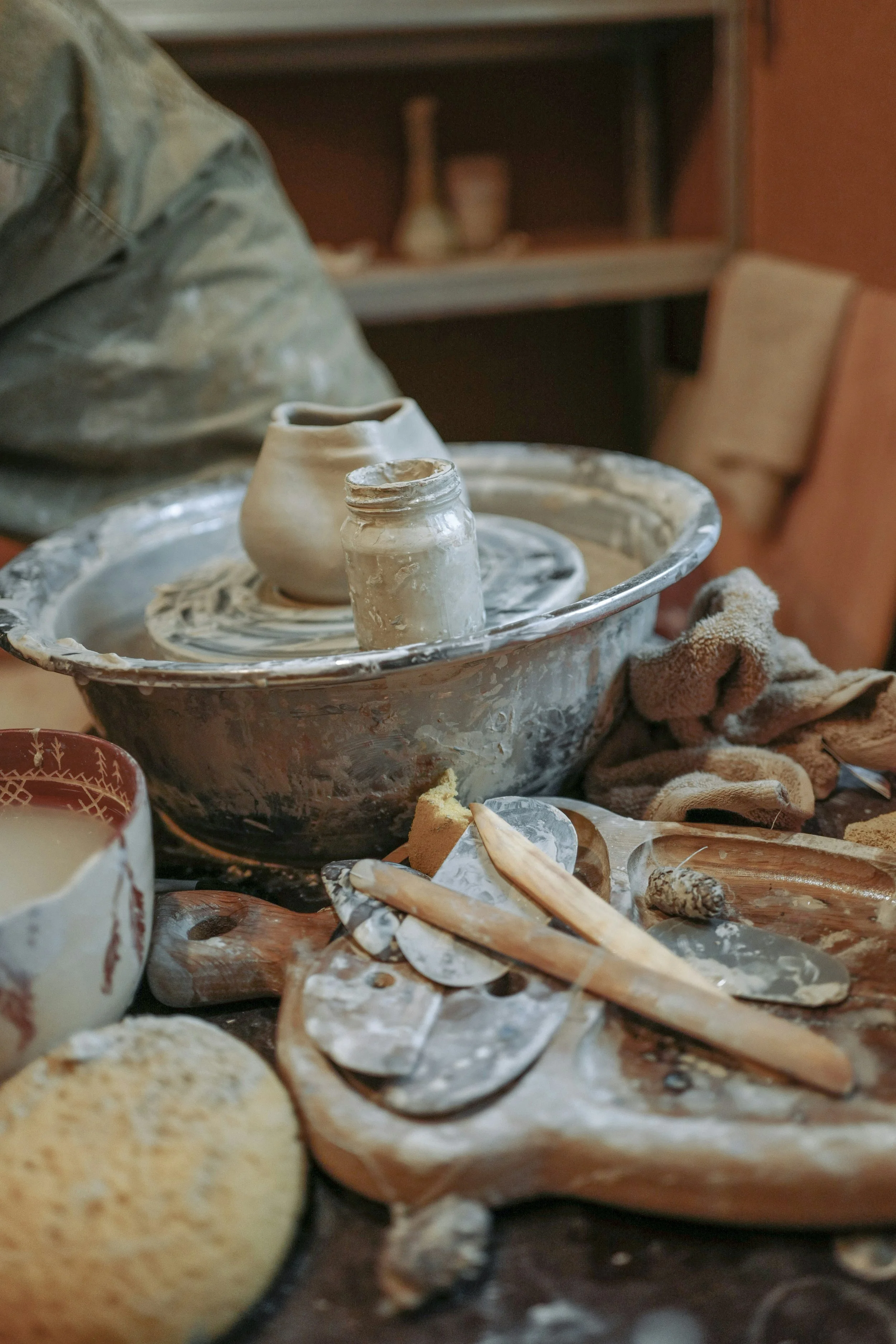 A pottery workspace with clay projects, tools, and a bowl covered in clay residue, indicating an active ceramics or pottery making session.